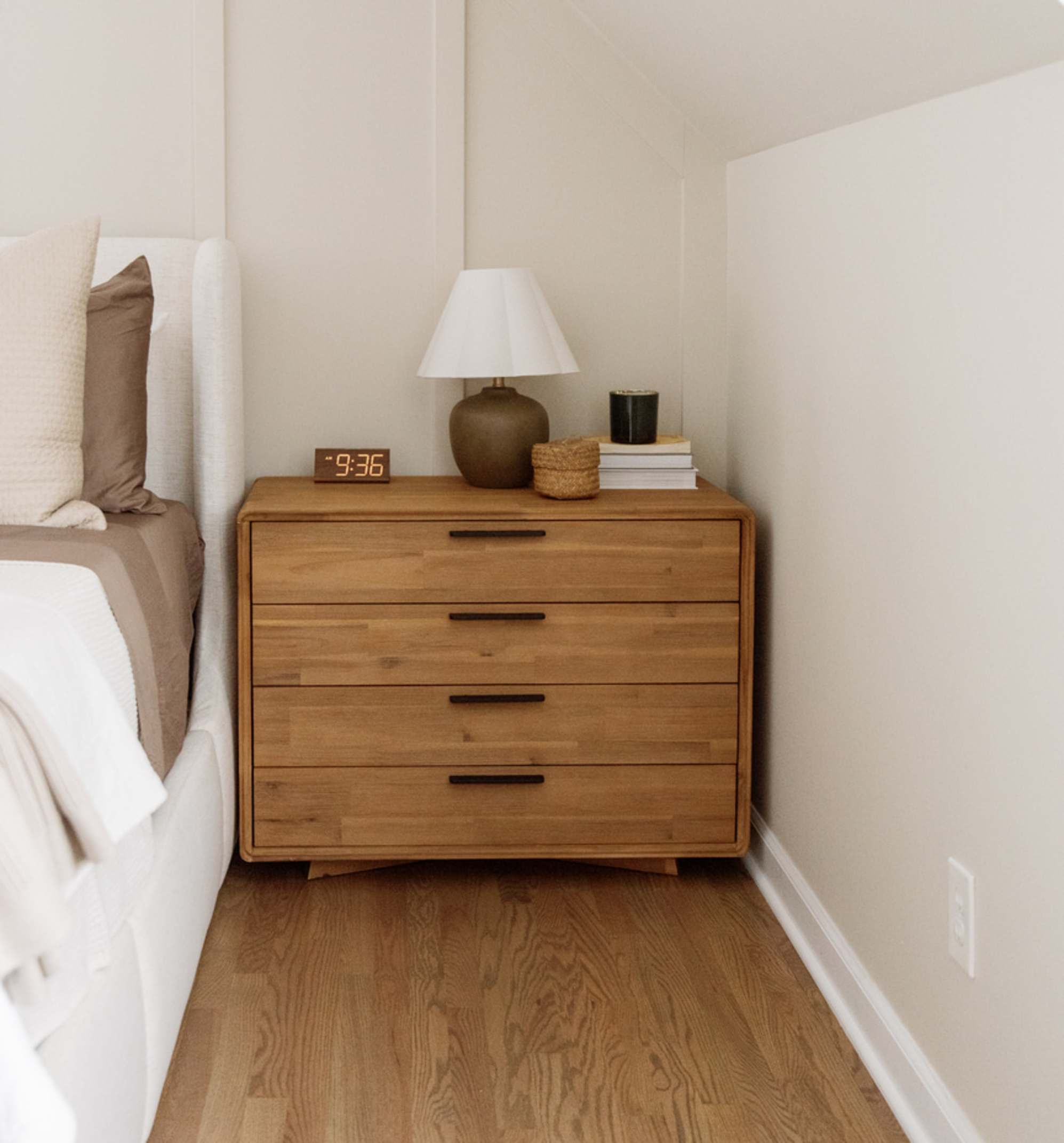 An acacia wood 4-drawer dresser placed beside a bed.