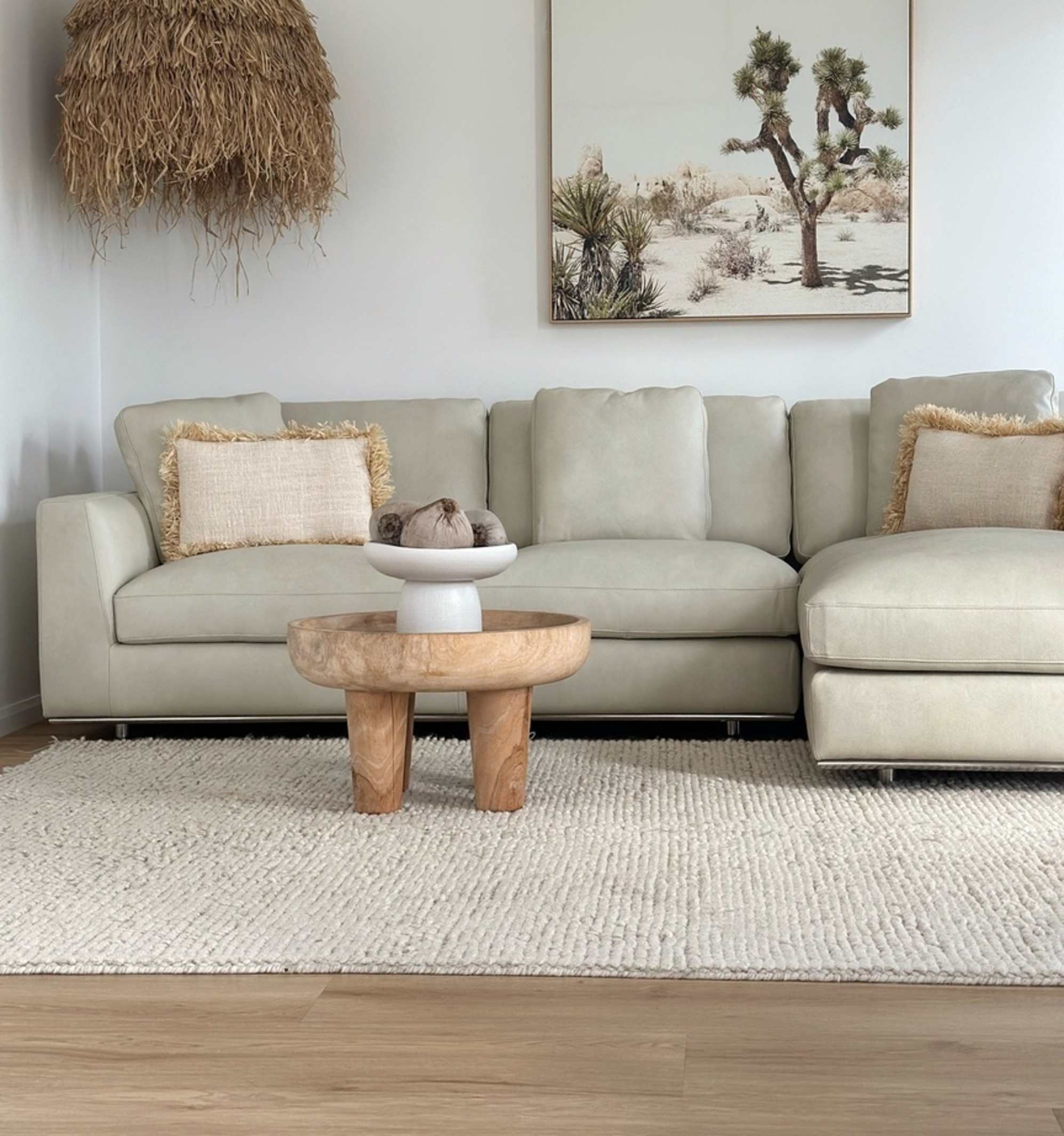 A white leather chaise sectional sofa placed in a living room with a large painting hanging behind it.