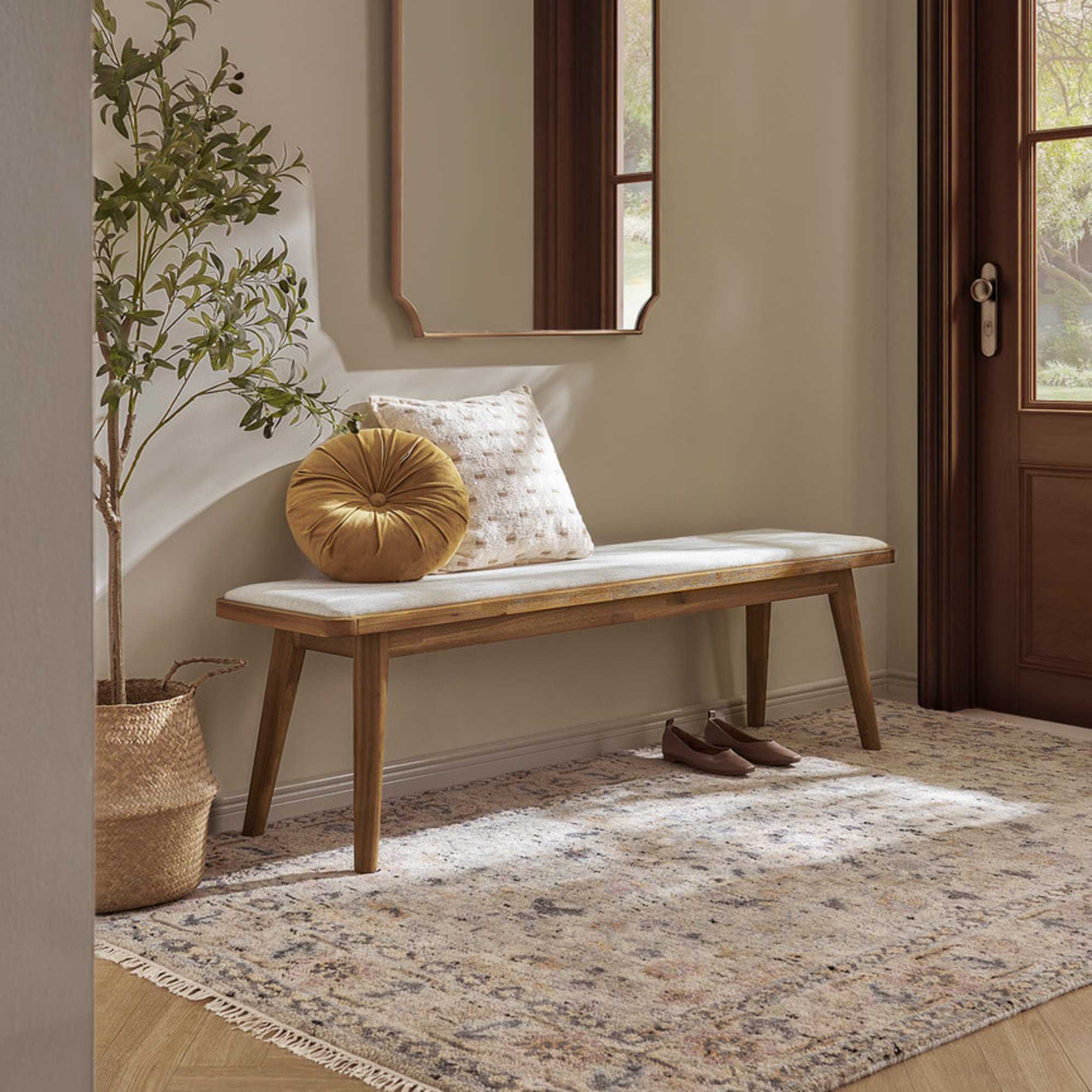 An acacia wood upholstered dining bench placed below a wall mirror by the door.