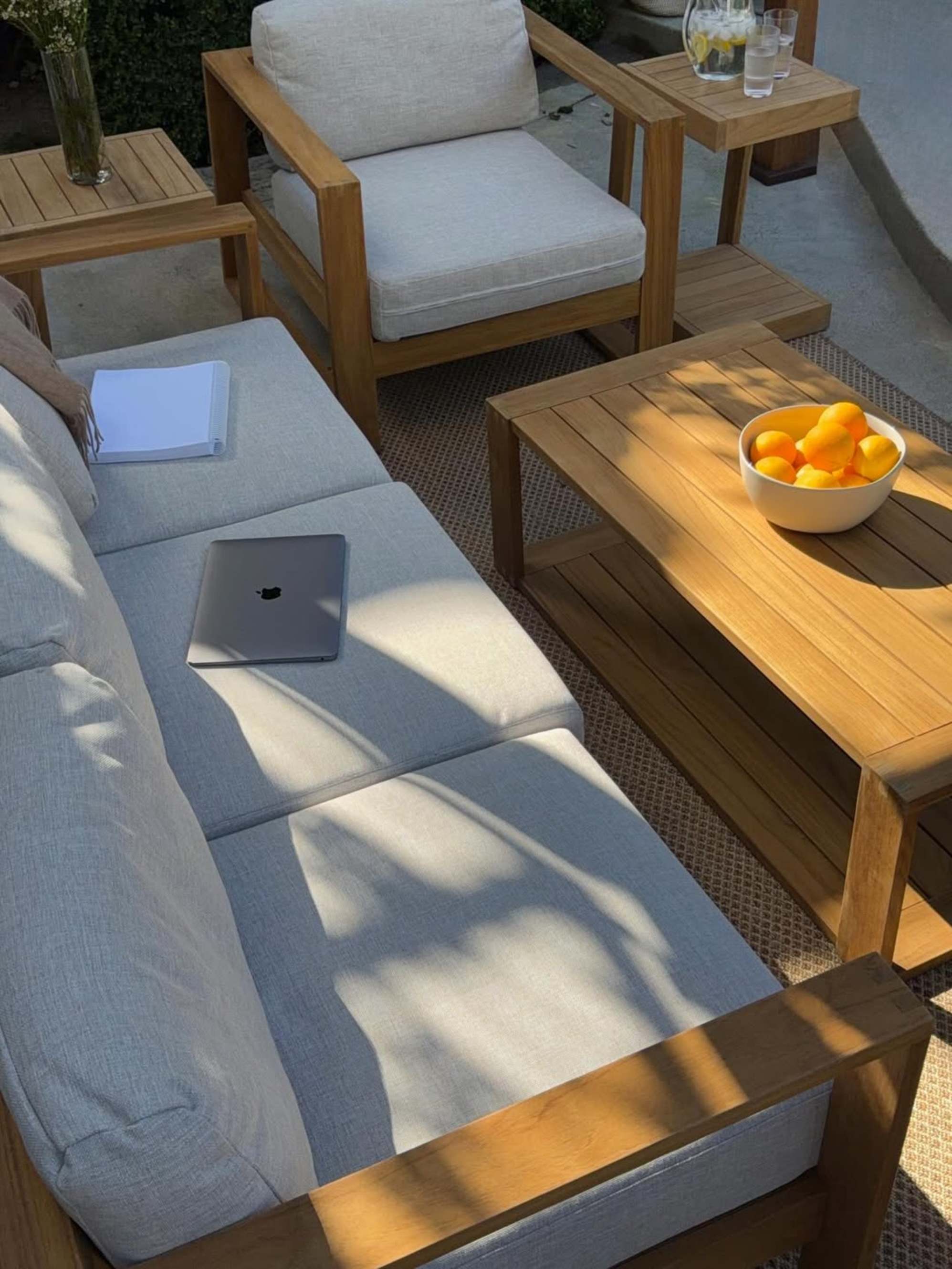 A teak outdoor sofa, coffee table, and lounge chair placed in the backyard.