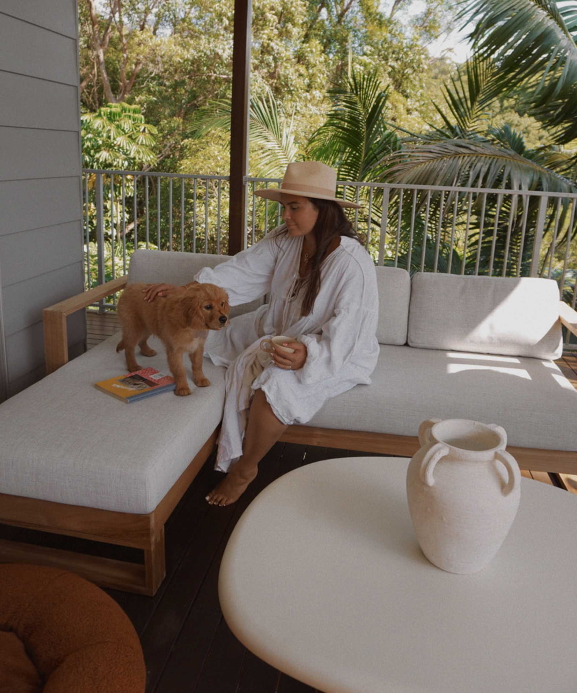 A person patting a dog on a teak outdoor chaise sectional sofa placed on a deck.