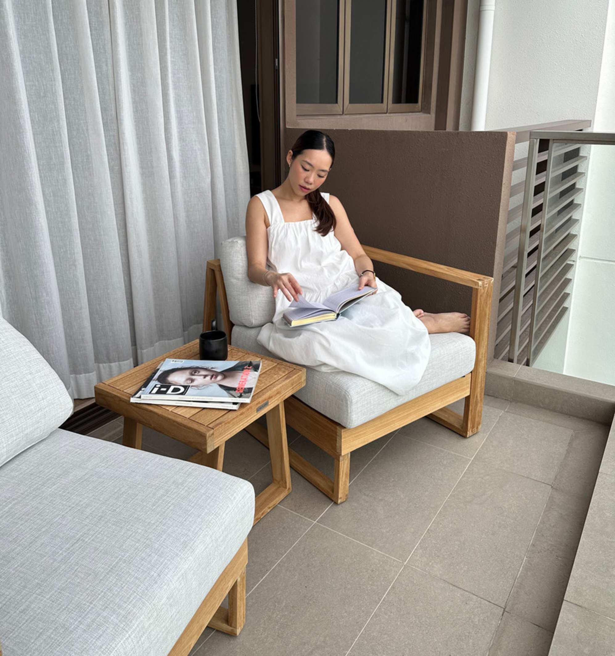 A person sitting on an individual module of a teak sofa while reading a book.