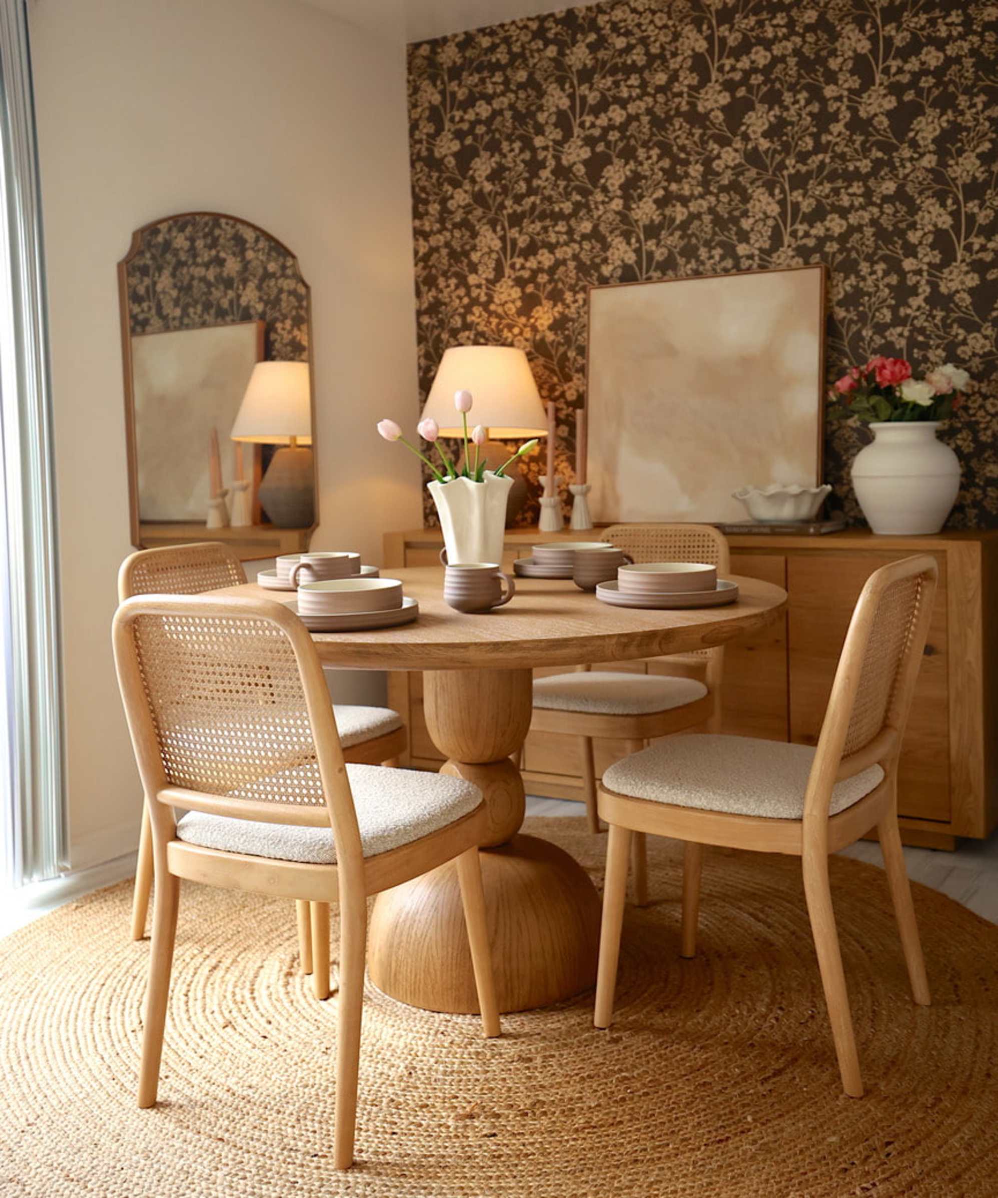 A round wooden dining table with a wall mirror placed on the wall beside the dinner table.
