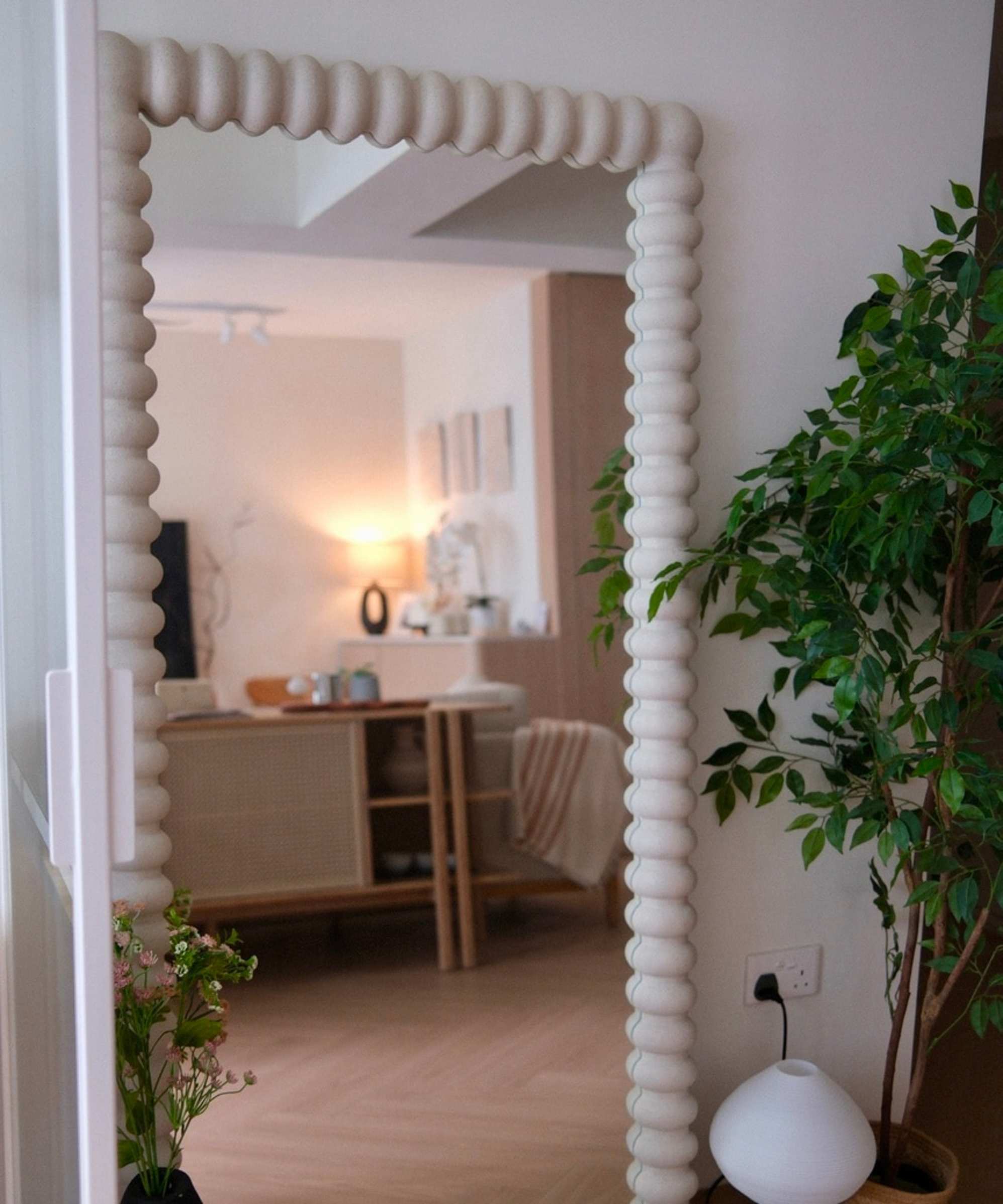 A sculptural floor mirror placed on the ground beside a plant.