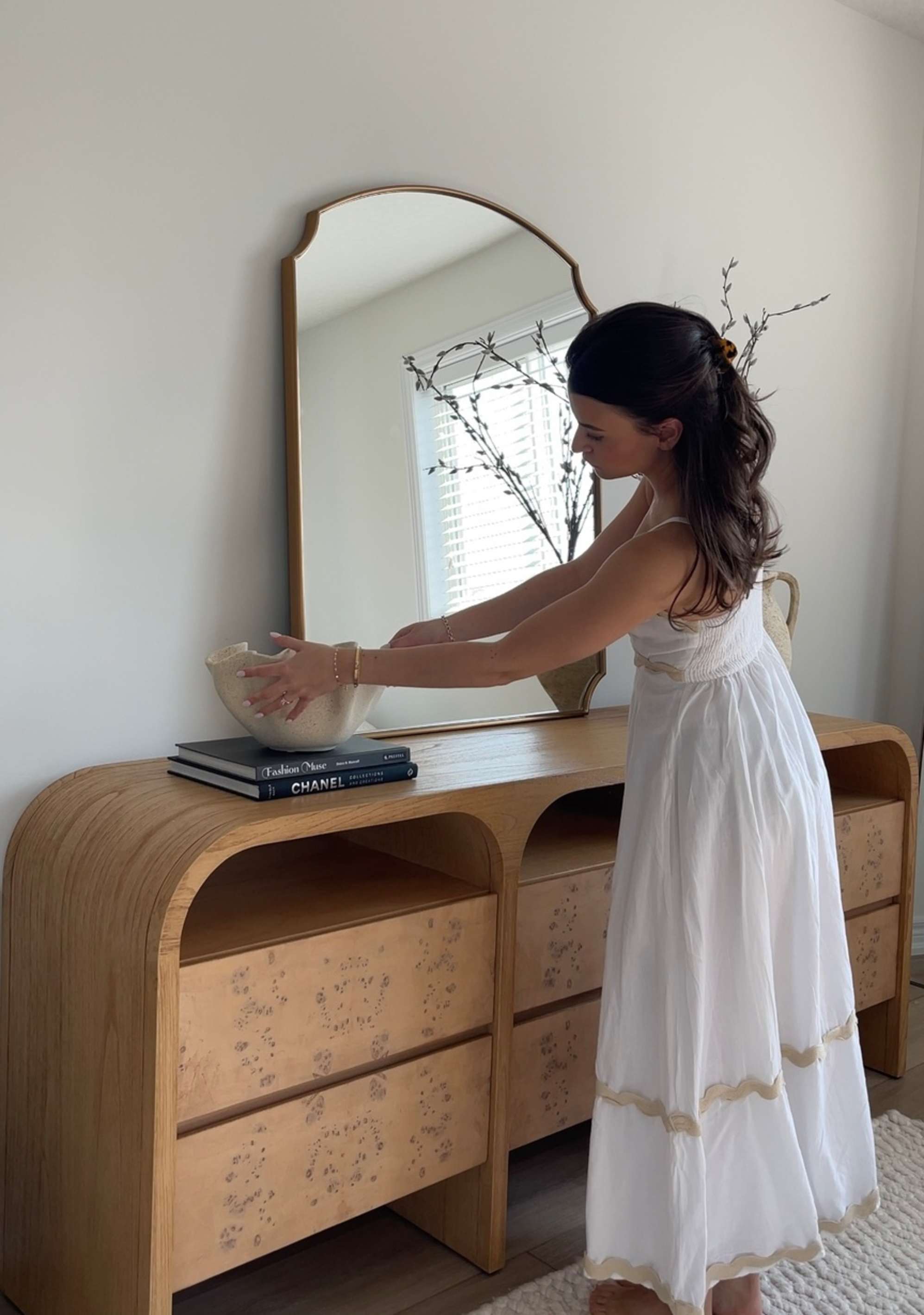 A person arranging a vase on a wooden sideboard.