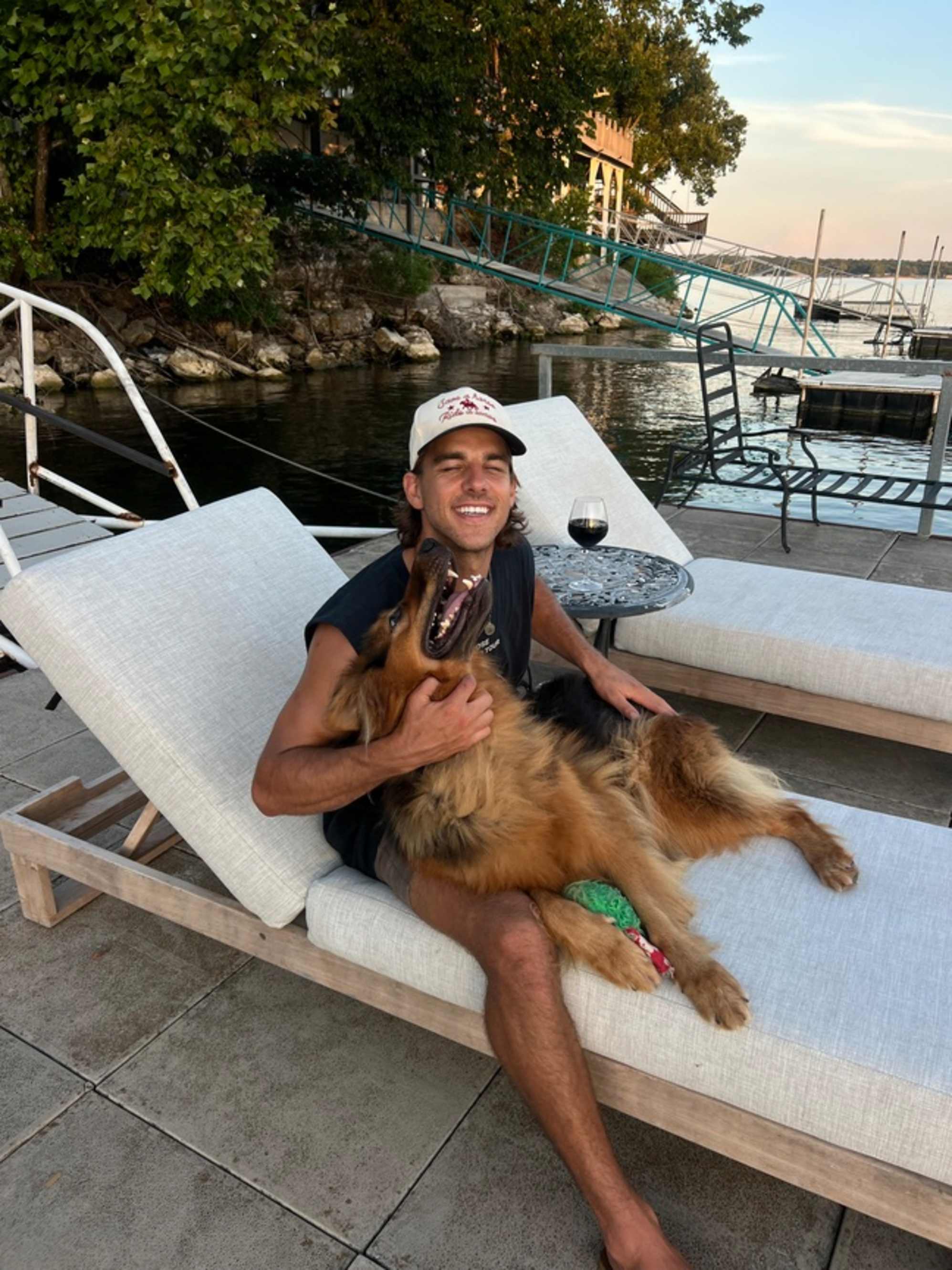 A man sitting on a chaise lounge while playing with a german shepard dog.