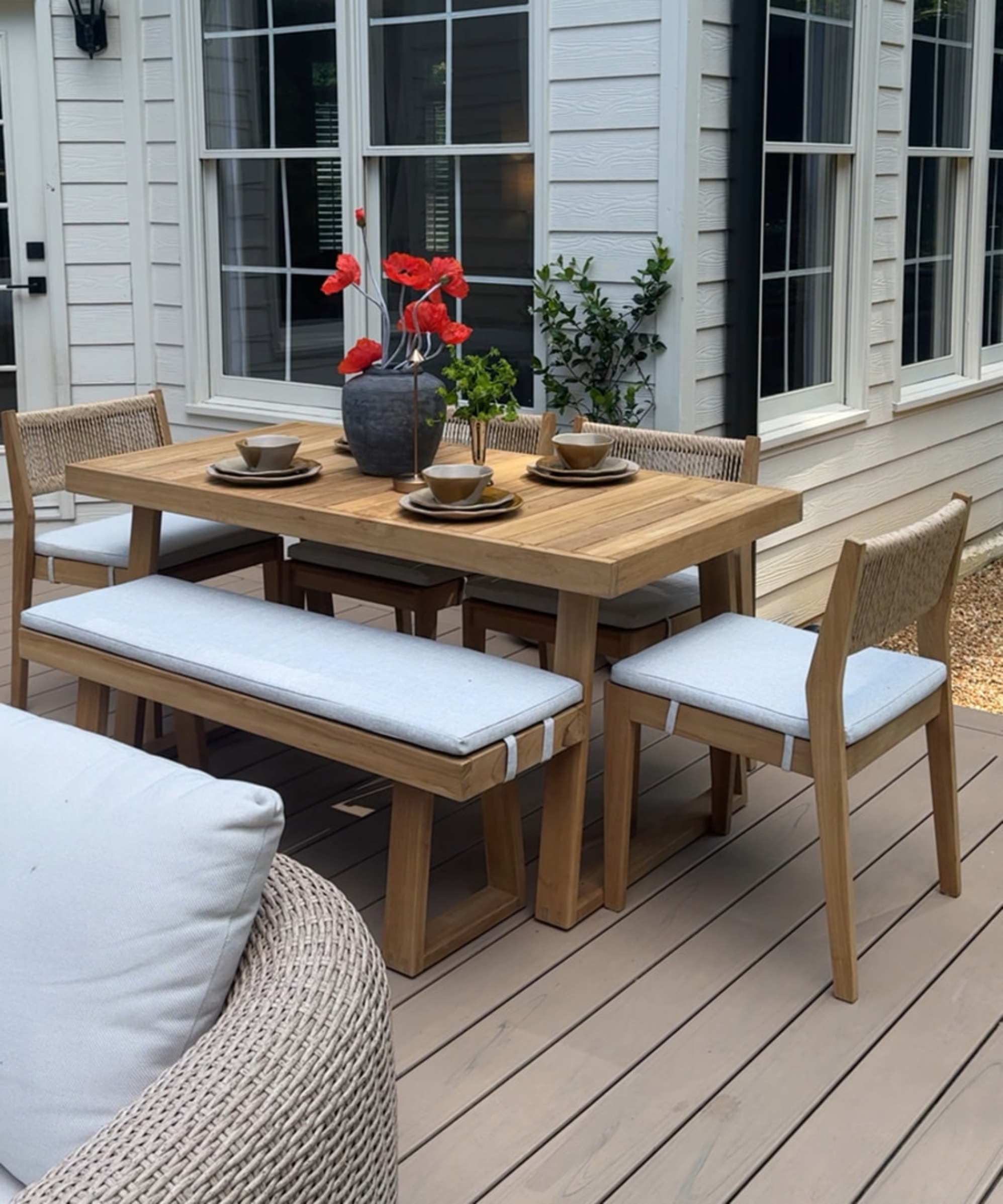A teak outdoor dining set placed on a deck in the backyard.