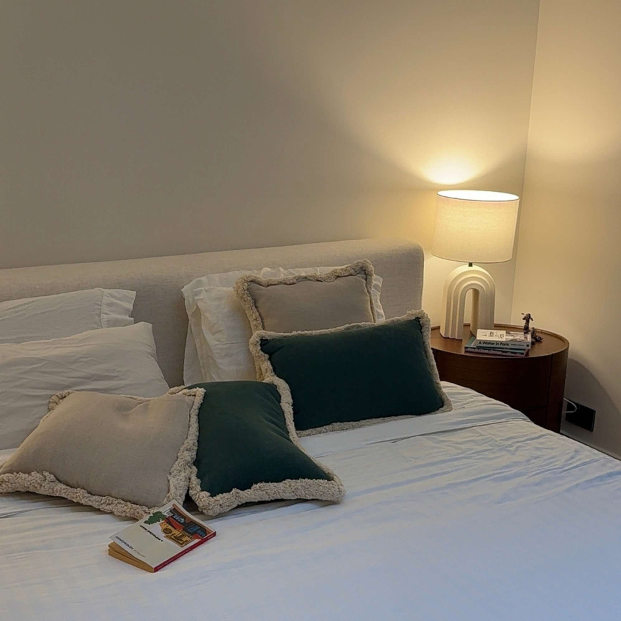 An arched table lamp with its light illuminating the bedside area.