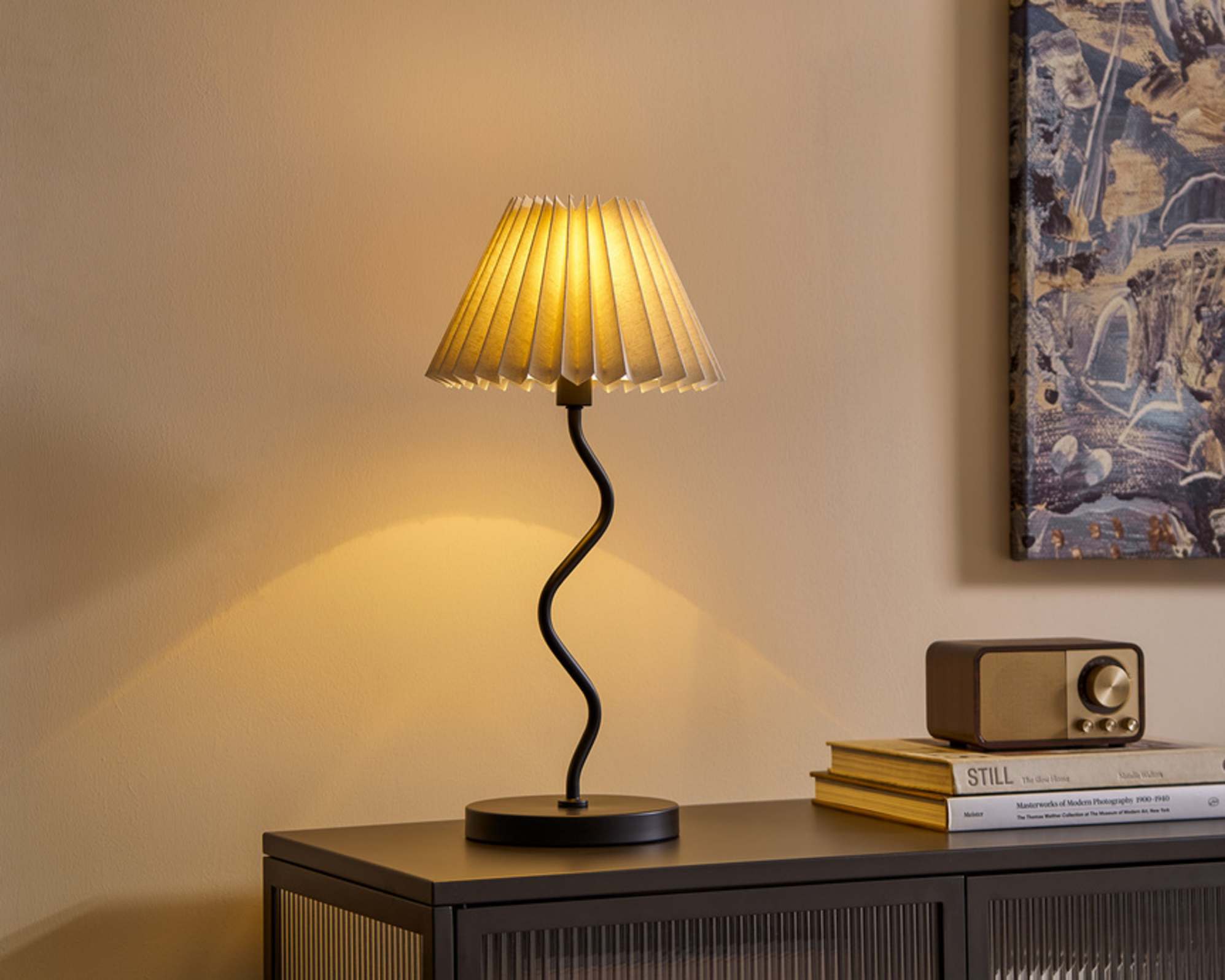 A table lamp with a wiggly steel base placed on a sideboard.