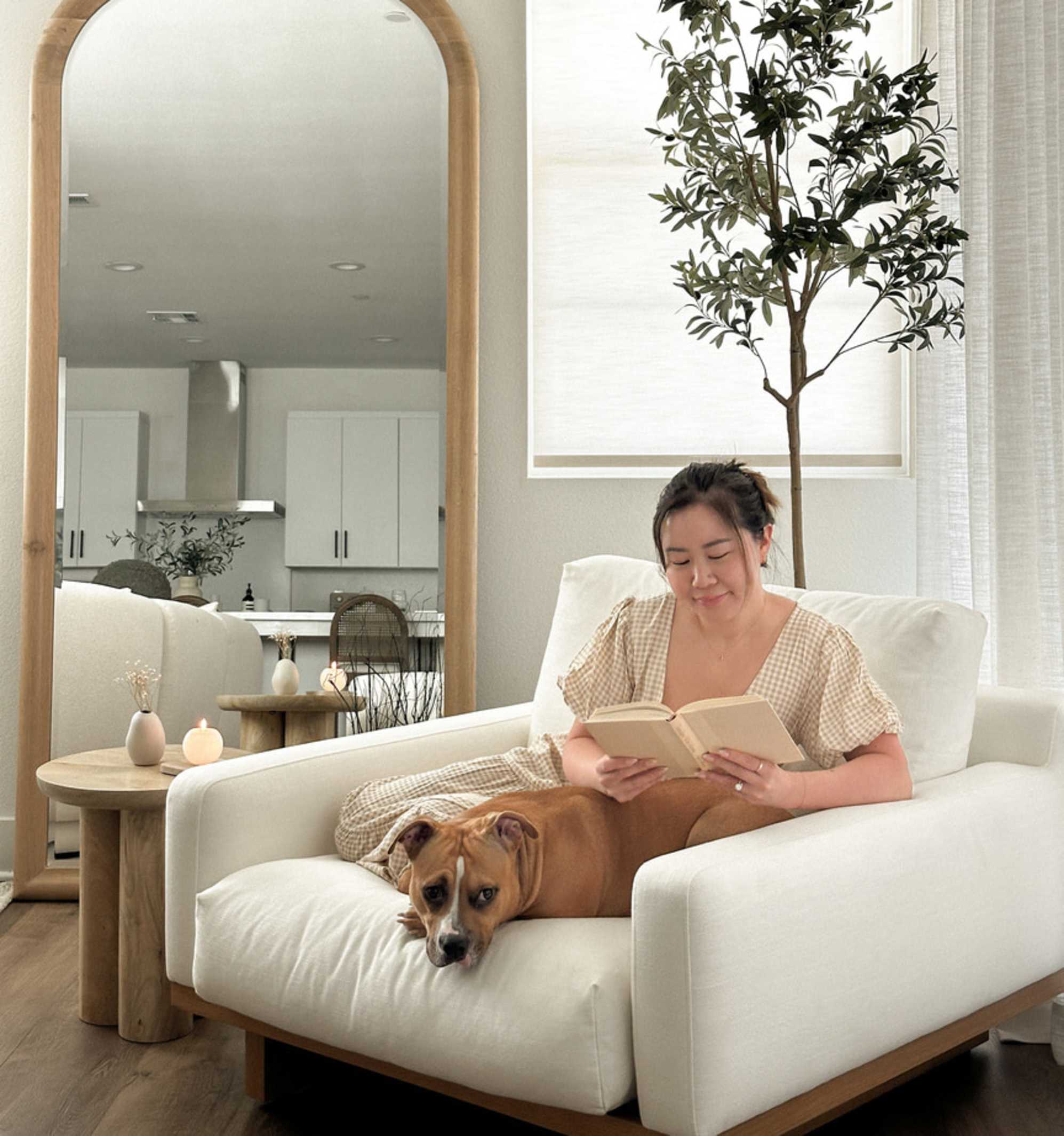 A person sitting on a performance fabric armchair with her dog while reading a book.