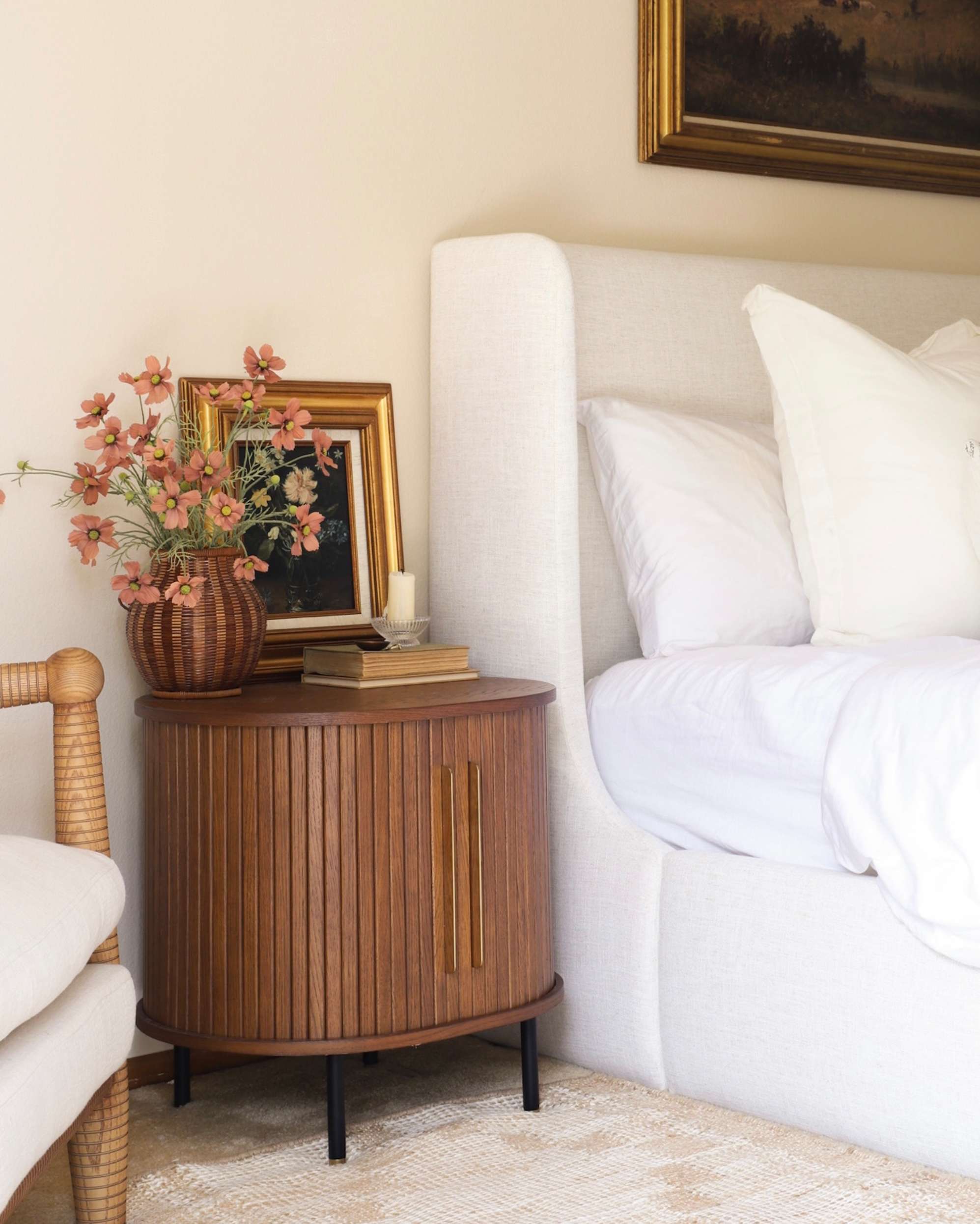 A decorated wooden bedside table by a white bed.
