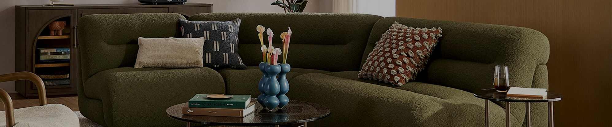 A moss green curved sofa placed in a living room with 3 throw pillows.