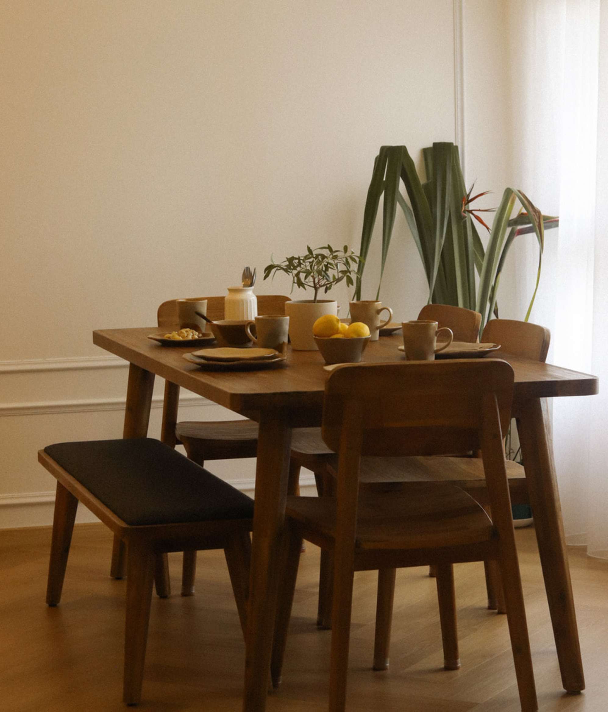 An acacia wood dining table with four dining chairs and an upholstered dining bench.