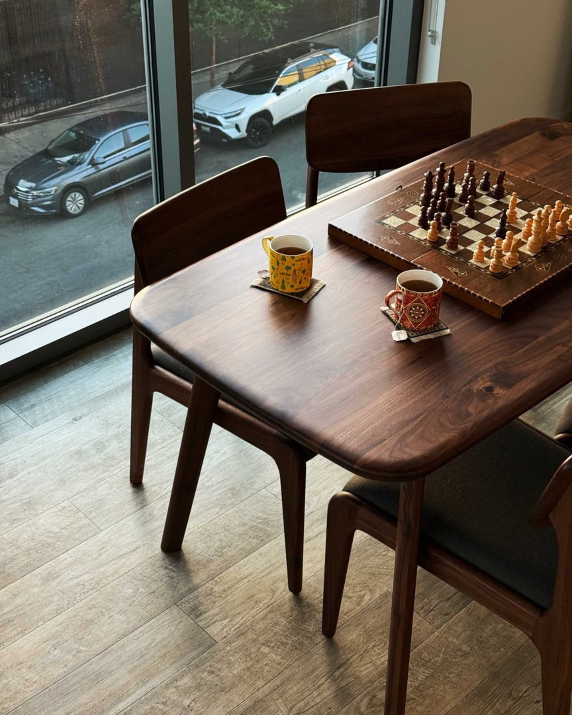 A walnut wood dining table with a chessboard and two mugs of tea.