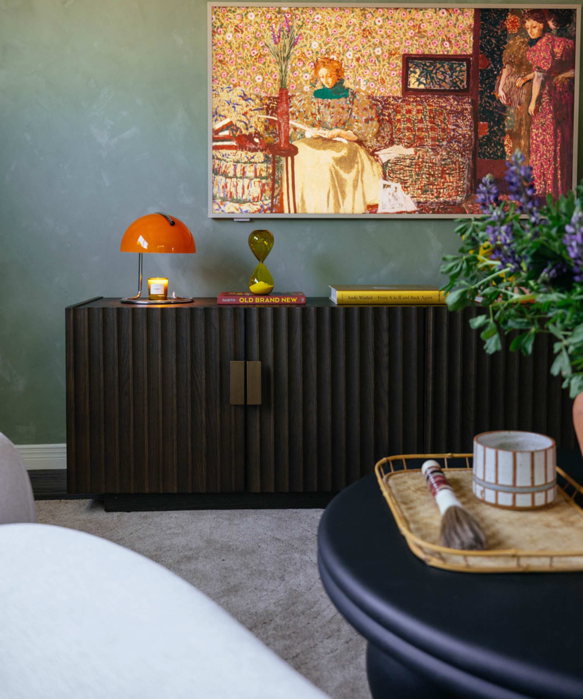 A black TV stand with an orange lamp and a large painting hanging on the wall behind it.