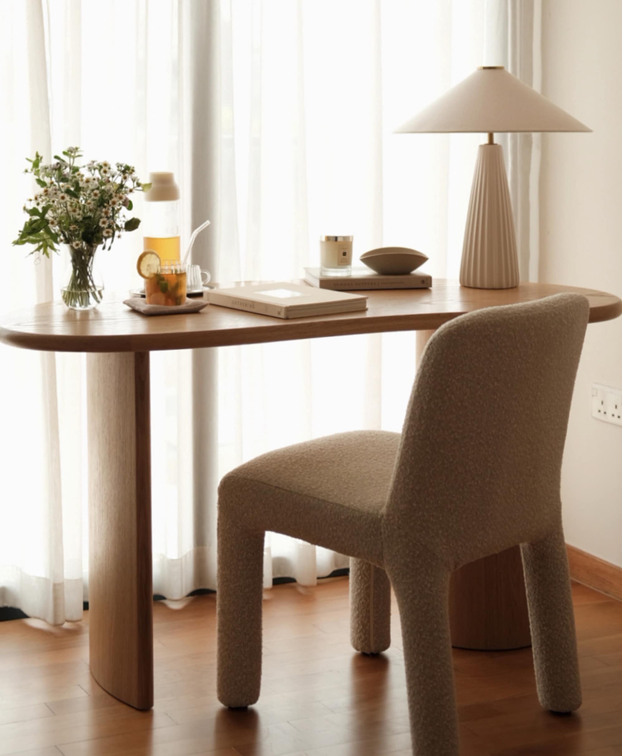 A curved desk placed in a room facing a window with sheer curtains.