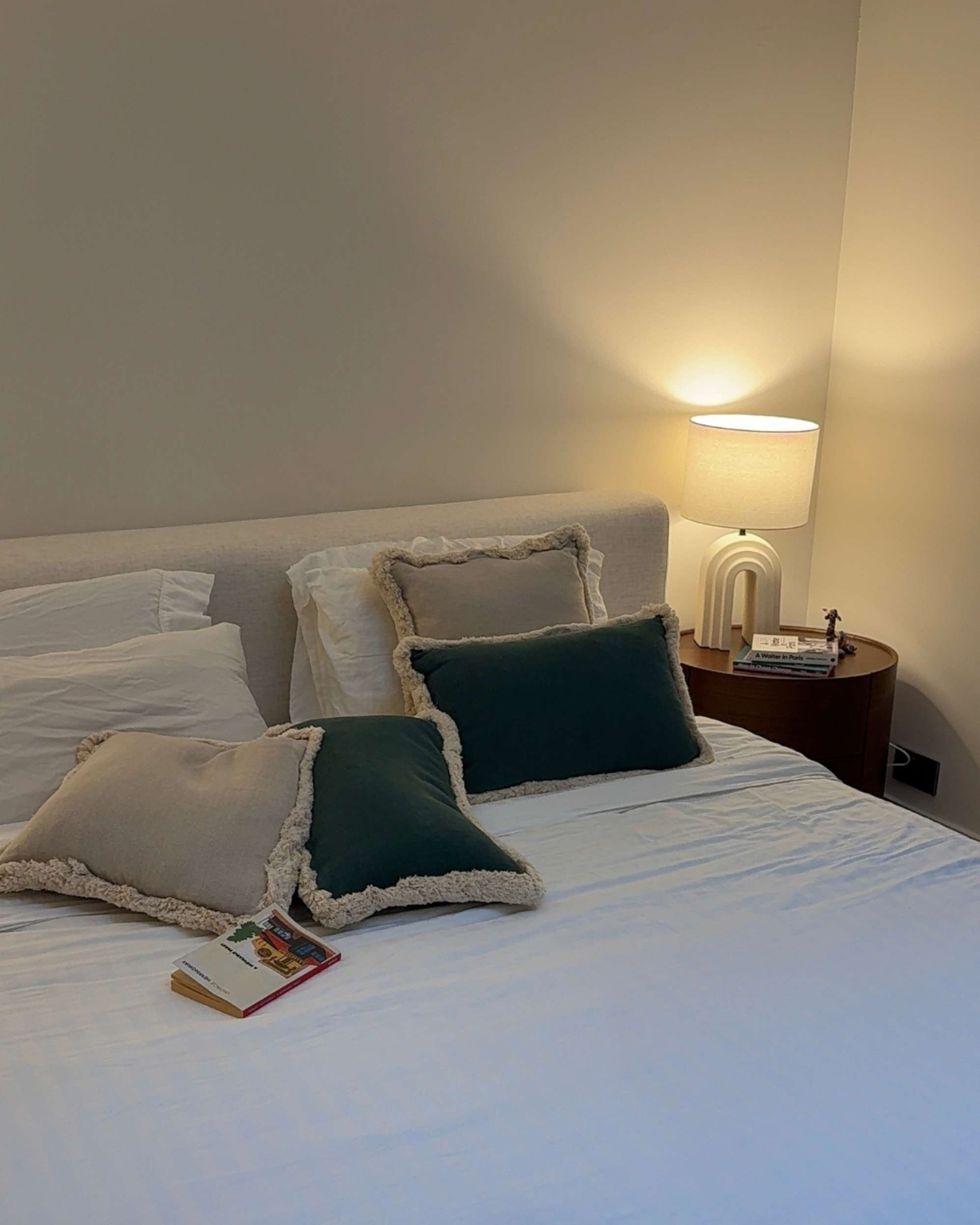 A lamp on a bedside table, beside a bed