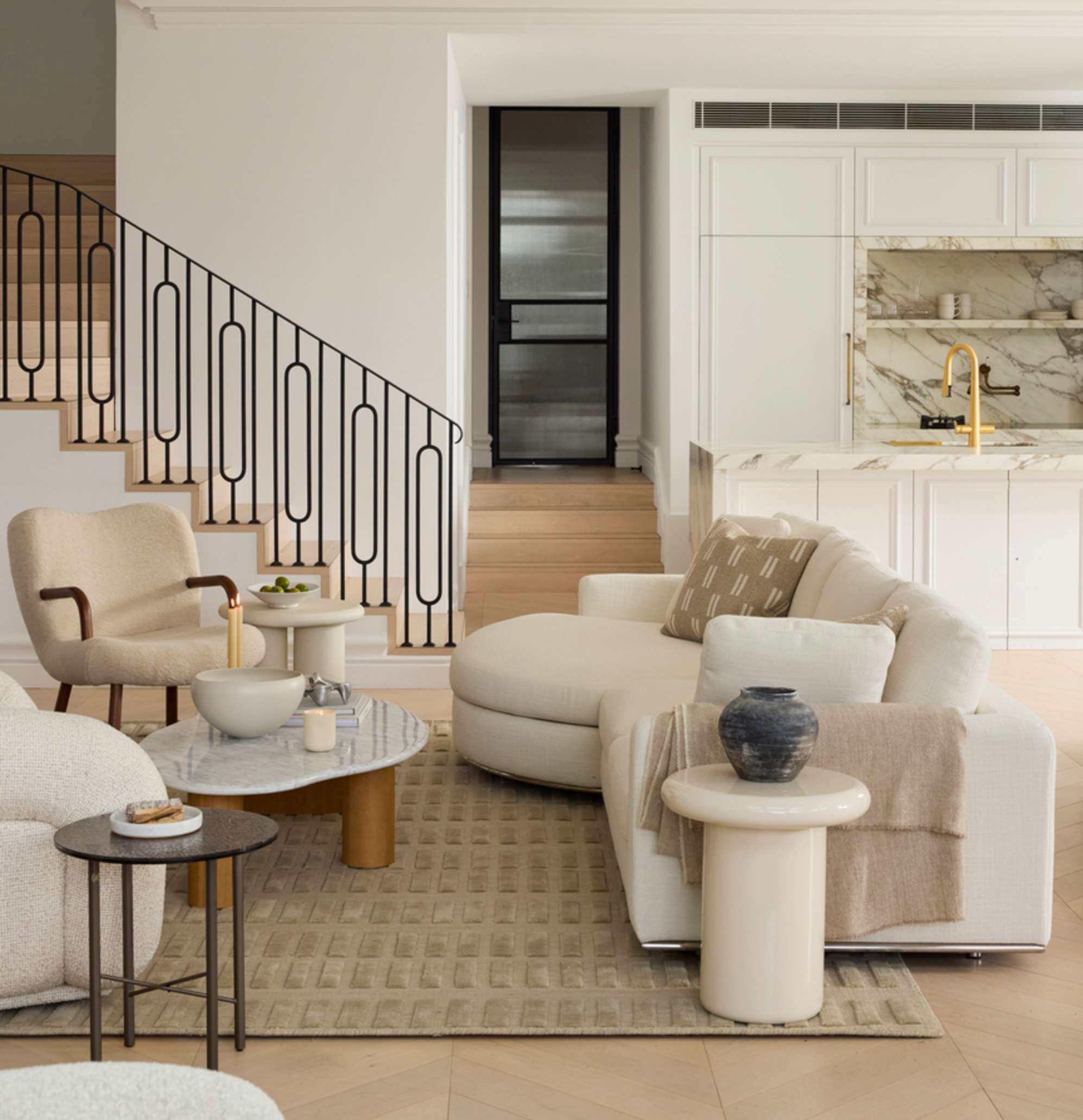 A round chaise sectional sofa with a marble coffee table and two armchairs placed opposite.