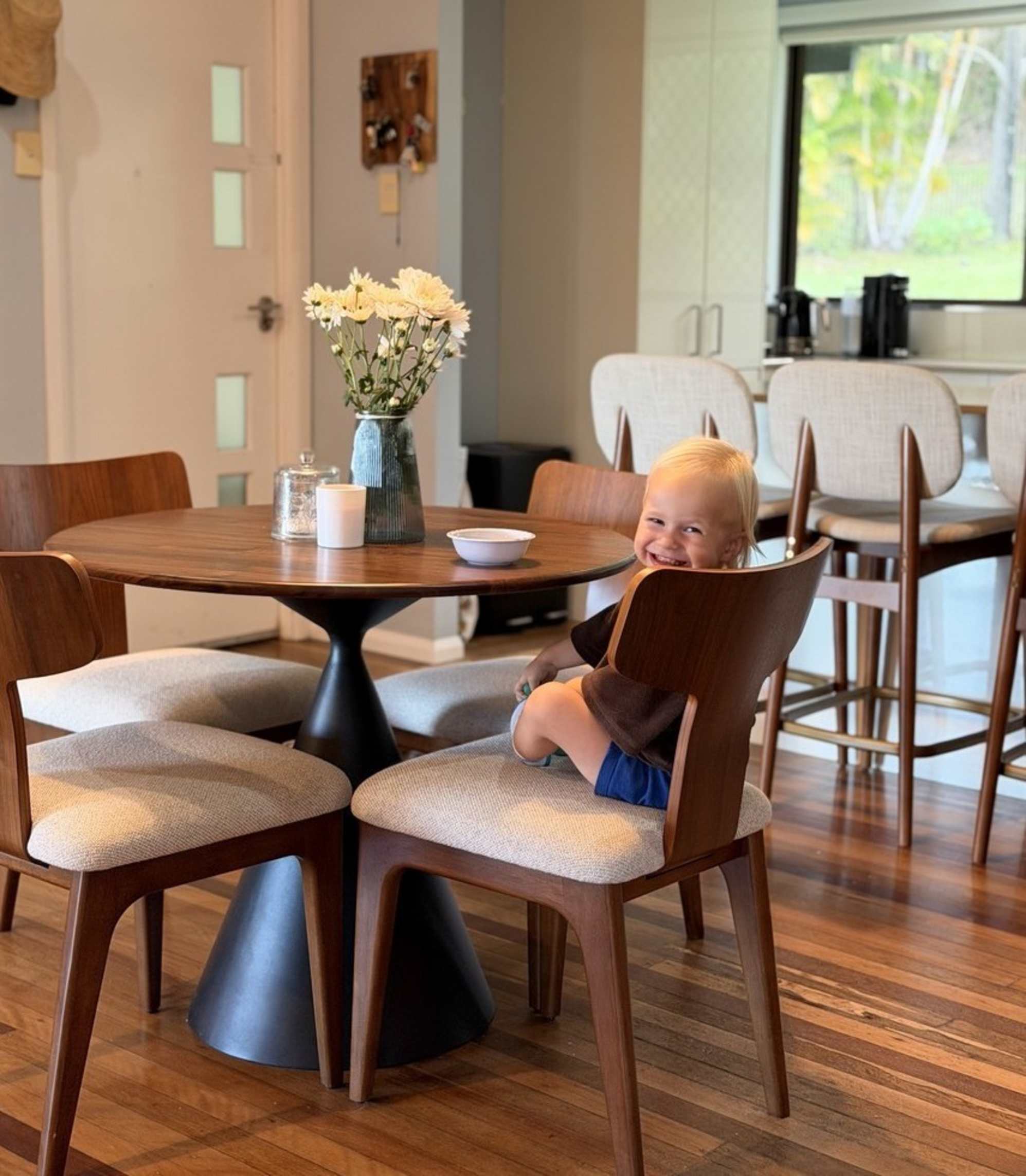A toddler sitting on a performance fabric dining chair at a round dining table.