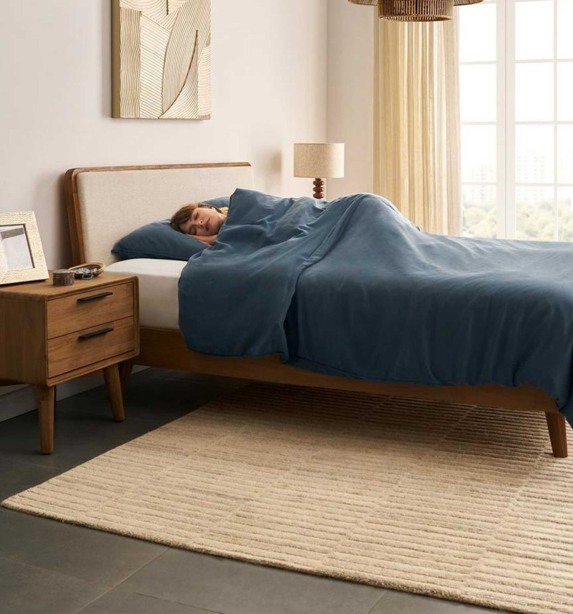 A person sleeping on her side on a bed with a deep blue duvet.