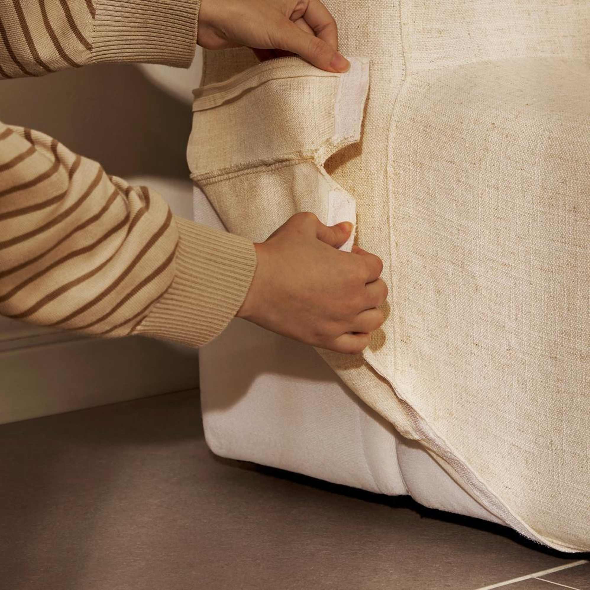 A person removing a cover from a machine-washable bed frame.