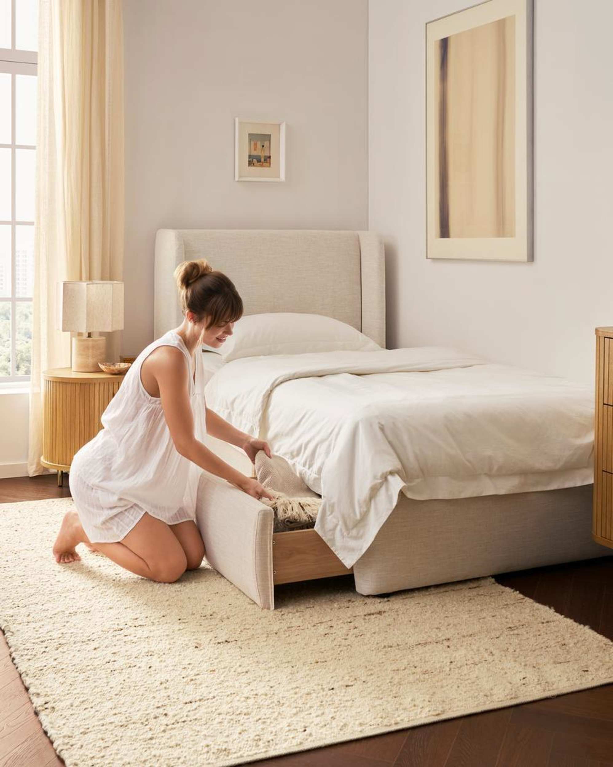 A woman keeping a throw in a built-in drawer of a storage bed.