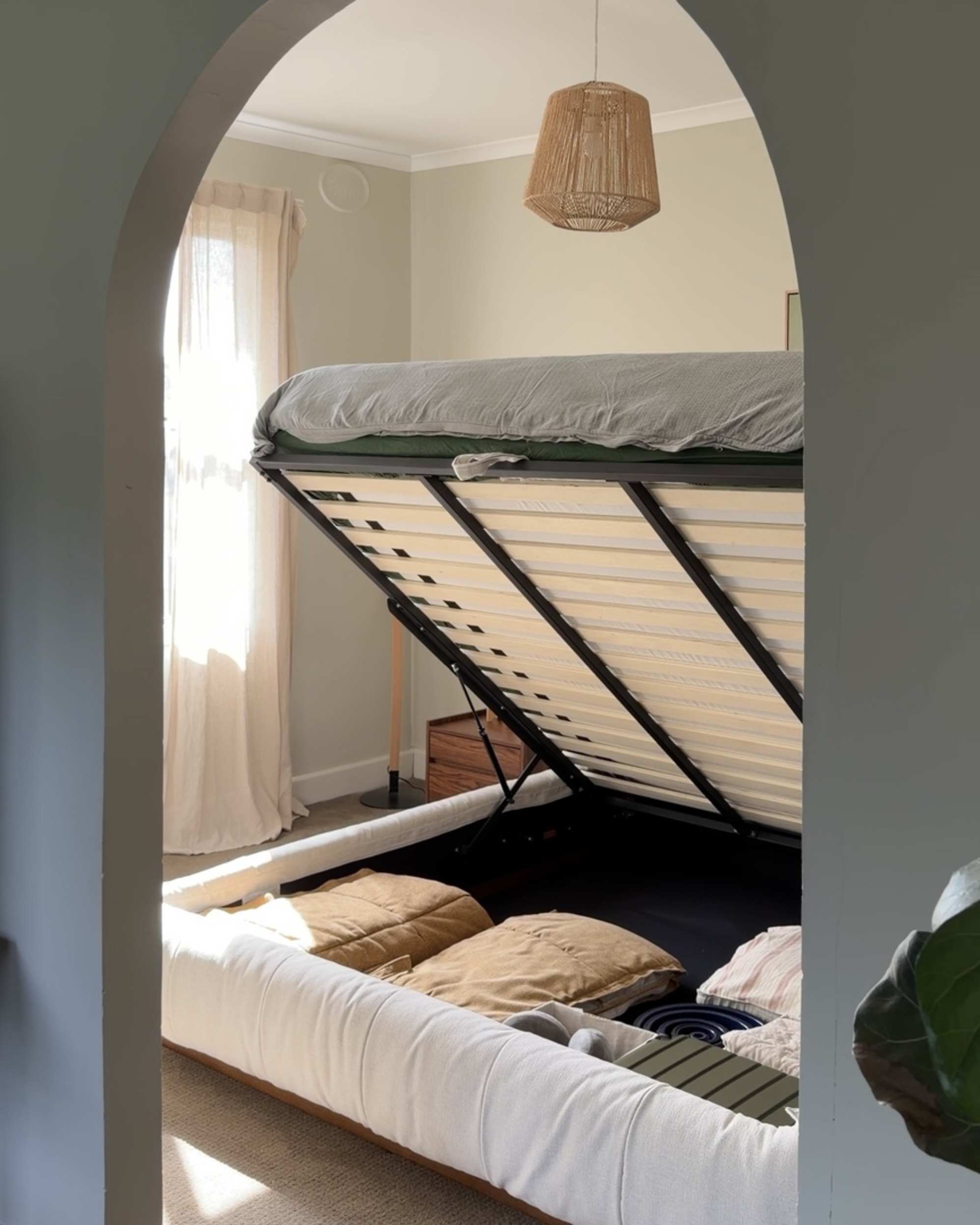 A gas-lift storage bed with its mattress lifted up to reveal bedding beneath.