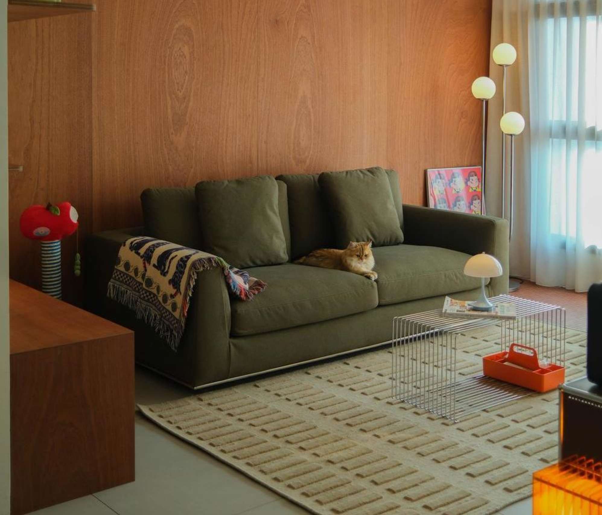 A cat sitting on a green sofa placed in a living room.