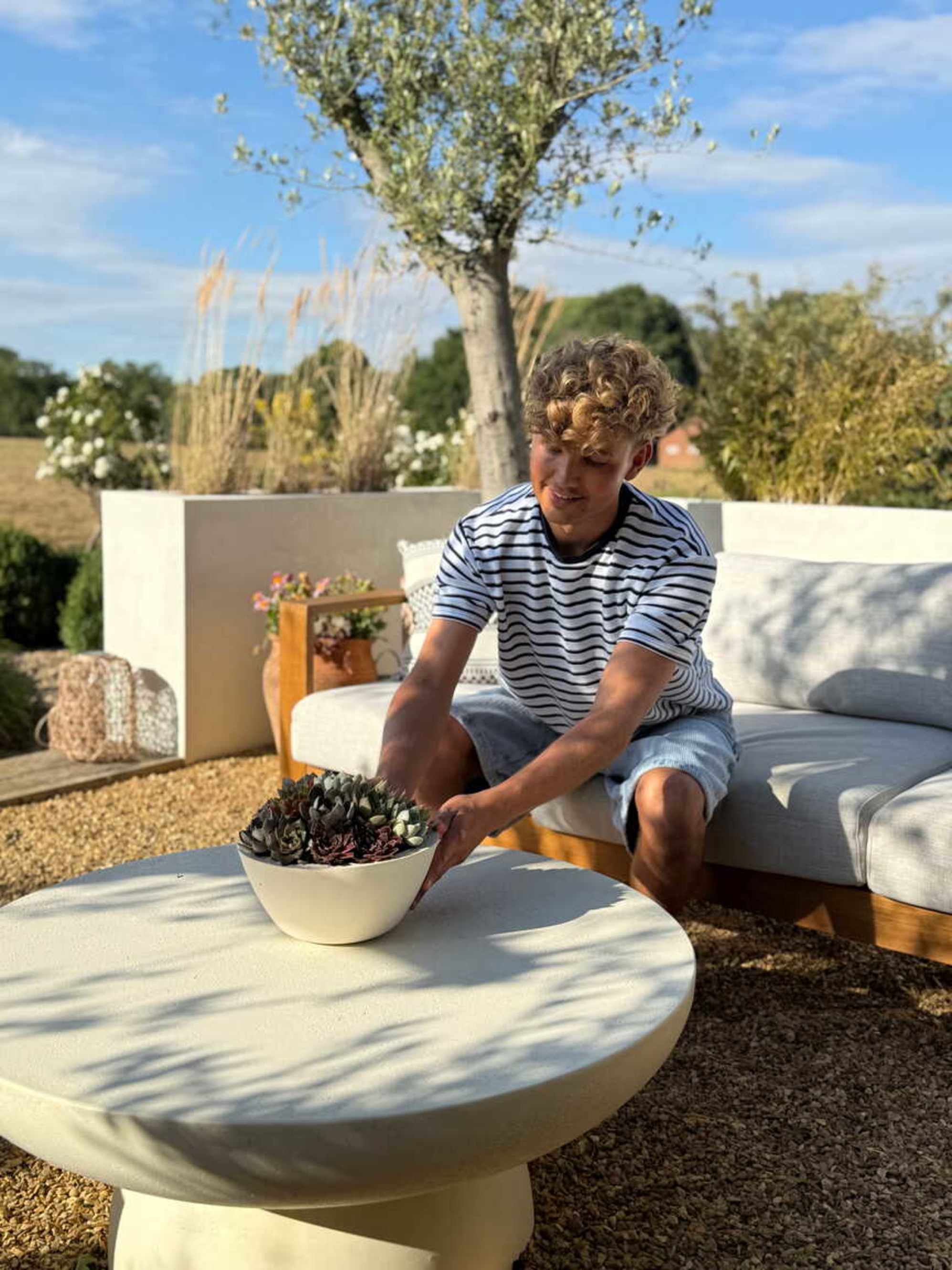 Jack Kinsey sitting on a teak outdoor sofa while holding a limestone planter he DIY-ed.