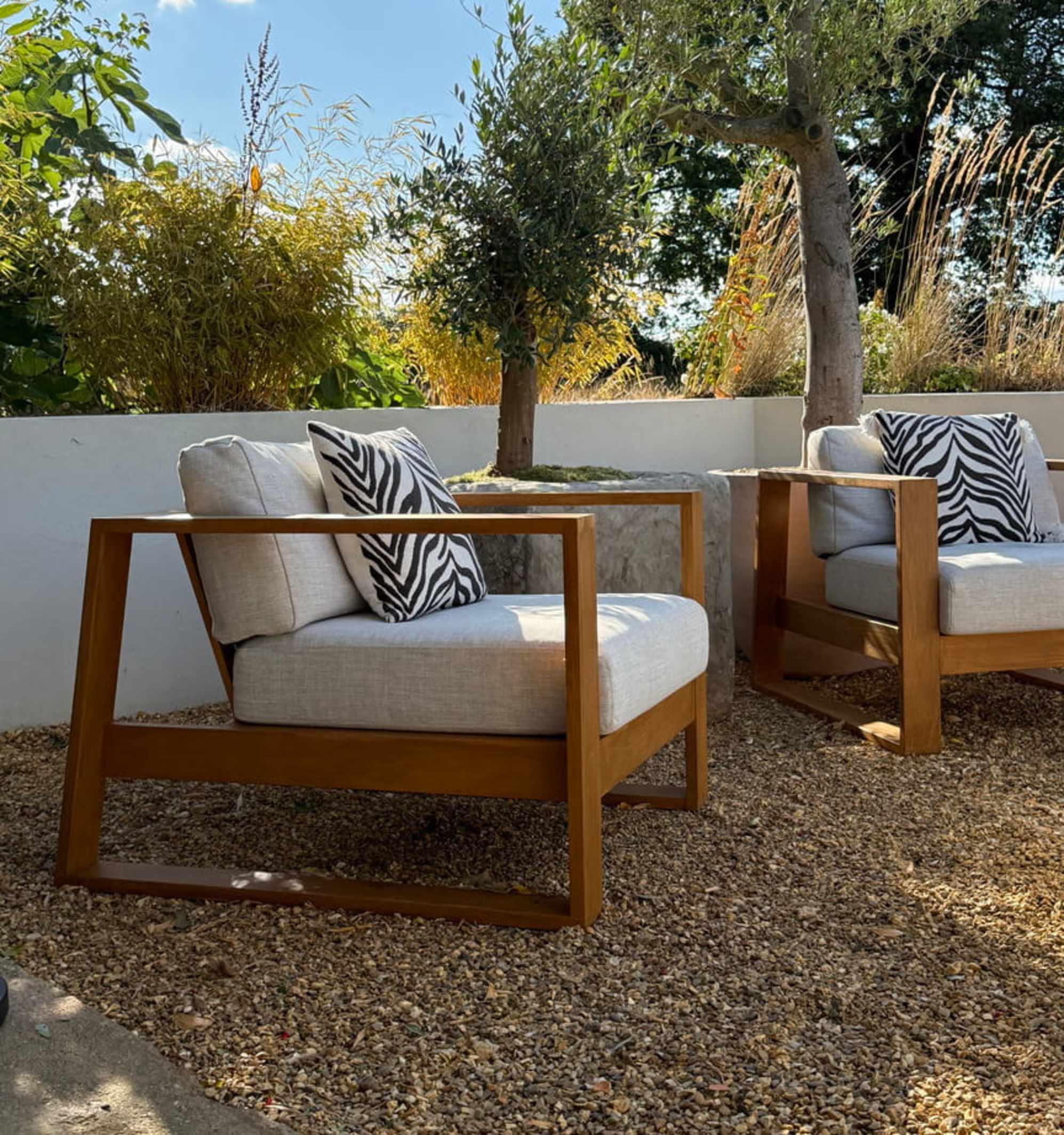 Two matching garden teak lounge chairs with a large planter placed between both chairs.