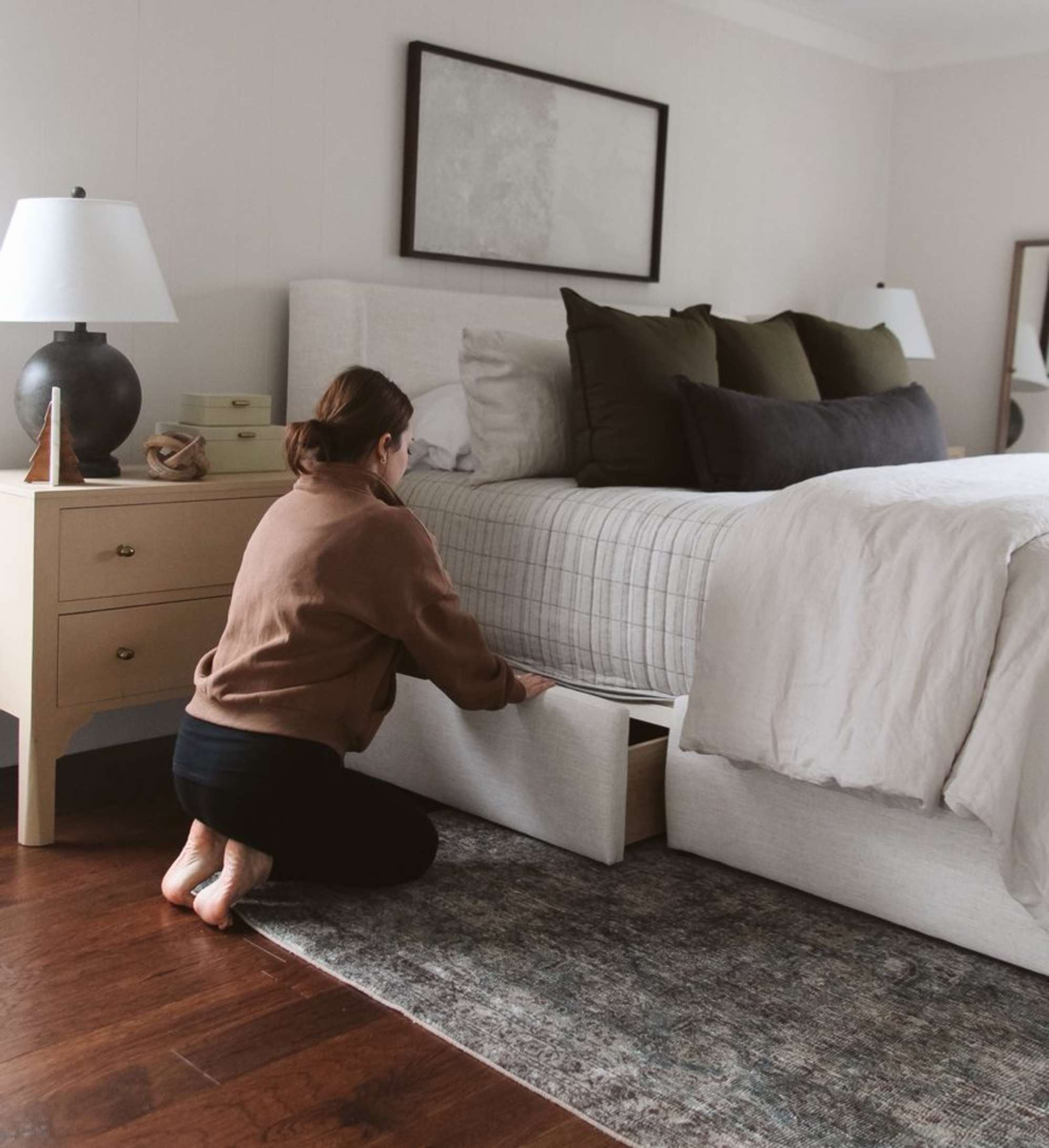 A person kneeling on the floor while opening a drawer compartment of a storage bed.
