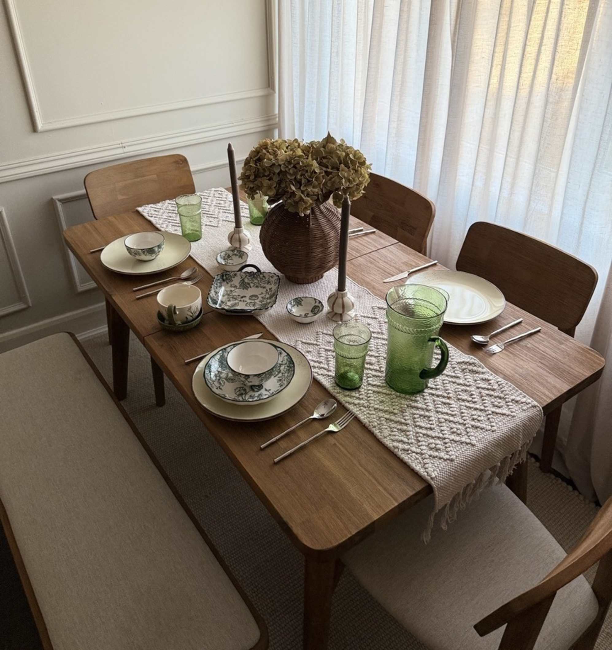 An acacia wood extendable dining table with matching wooden chairs and a bench.