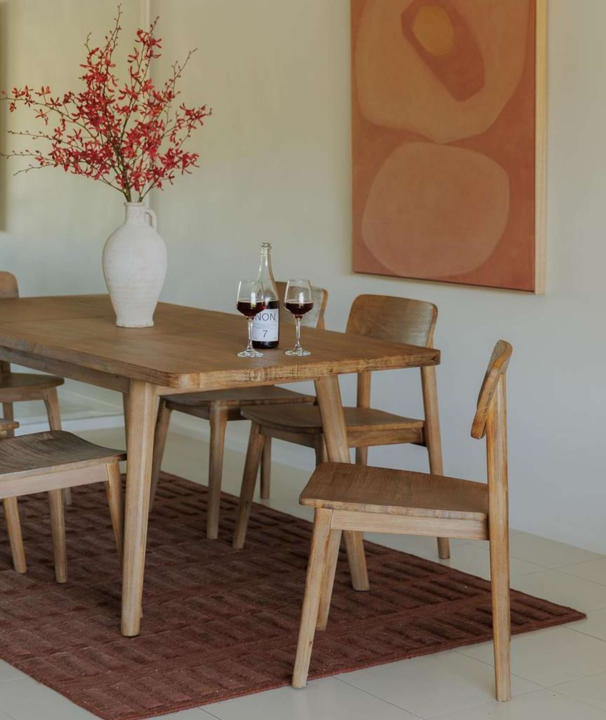 An extendable dining table with six acacia wood dining chairs placed on a brick red area rug.