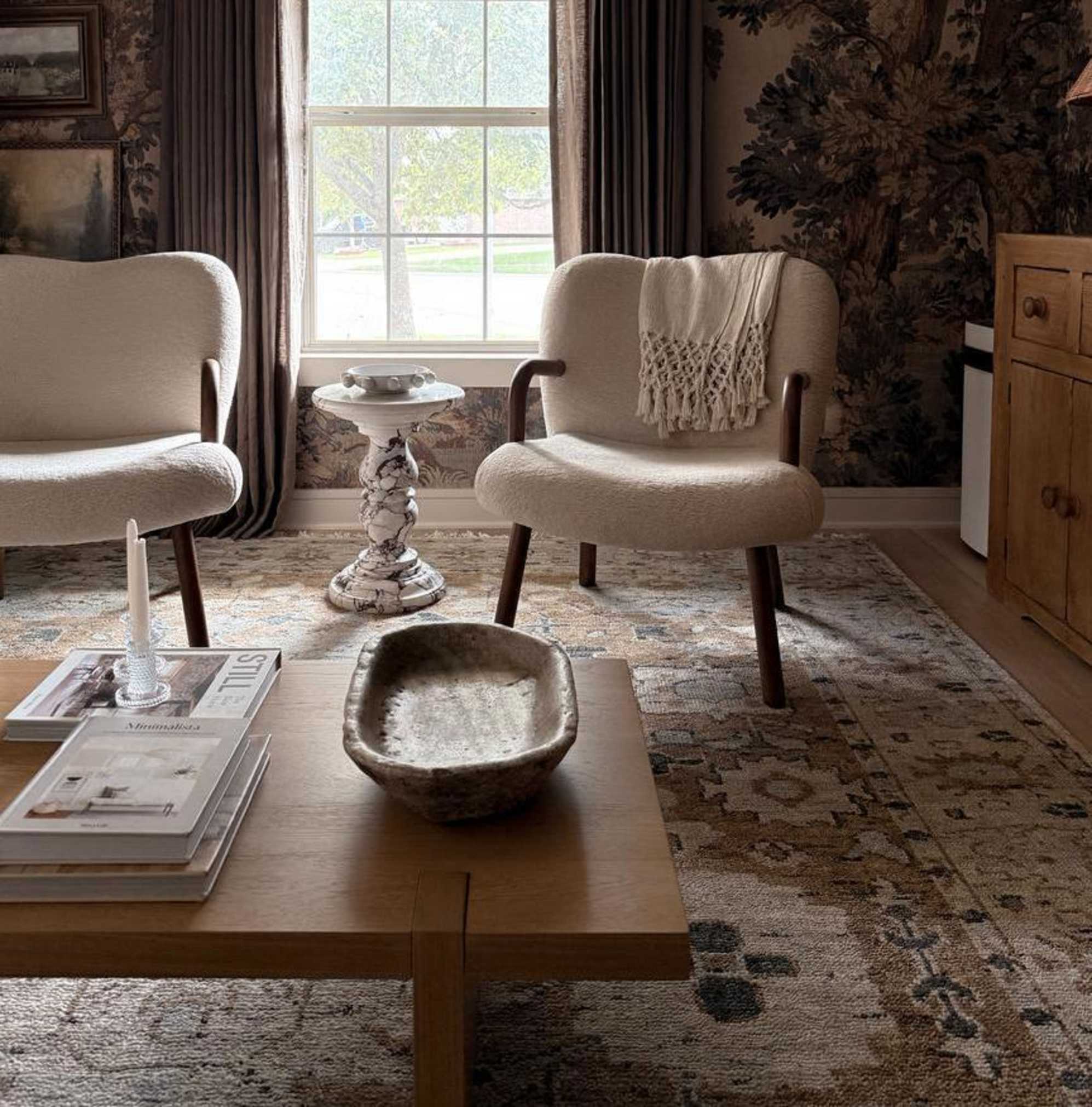 Two identical armchairs placed in front of a window with a white side table placed between them.