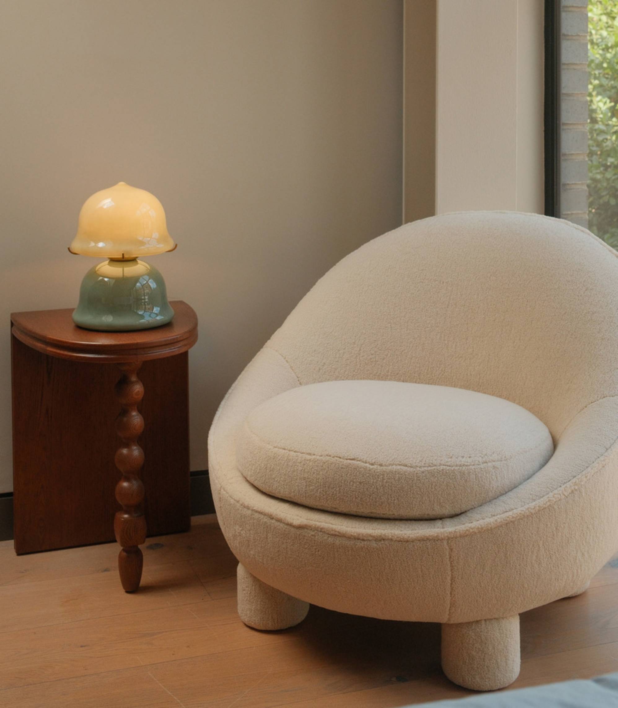 A round white armchair with a jade green table lamp placed on a wooden side table.