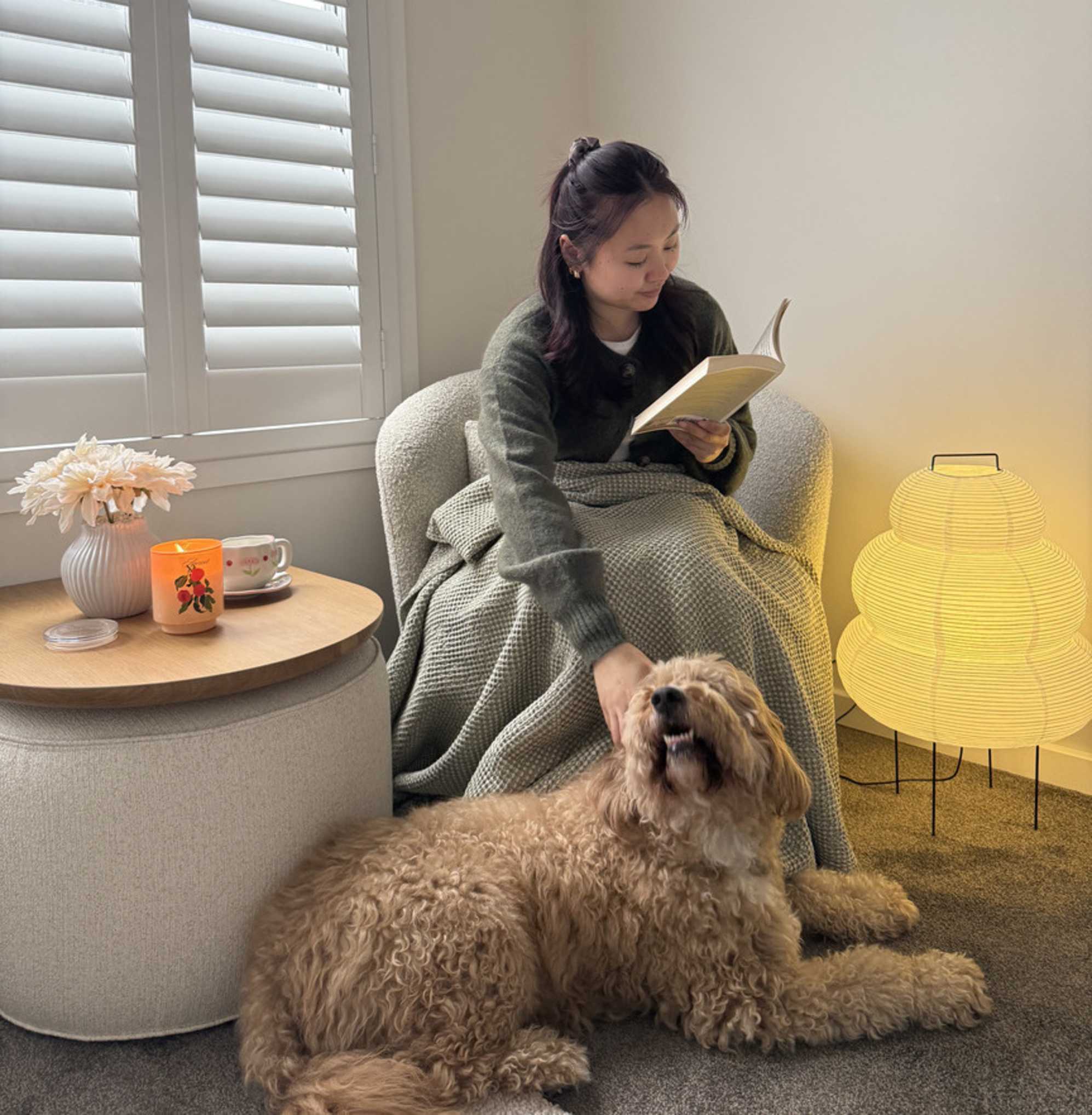 A woman sitting on a swivel chair while reading a book and petting her dog.