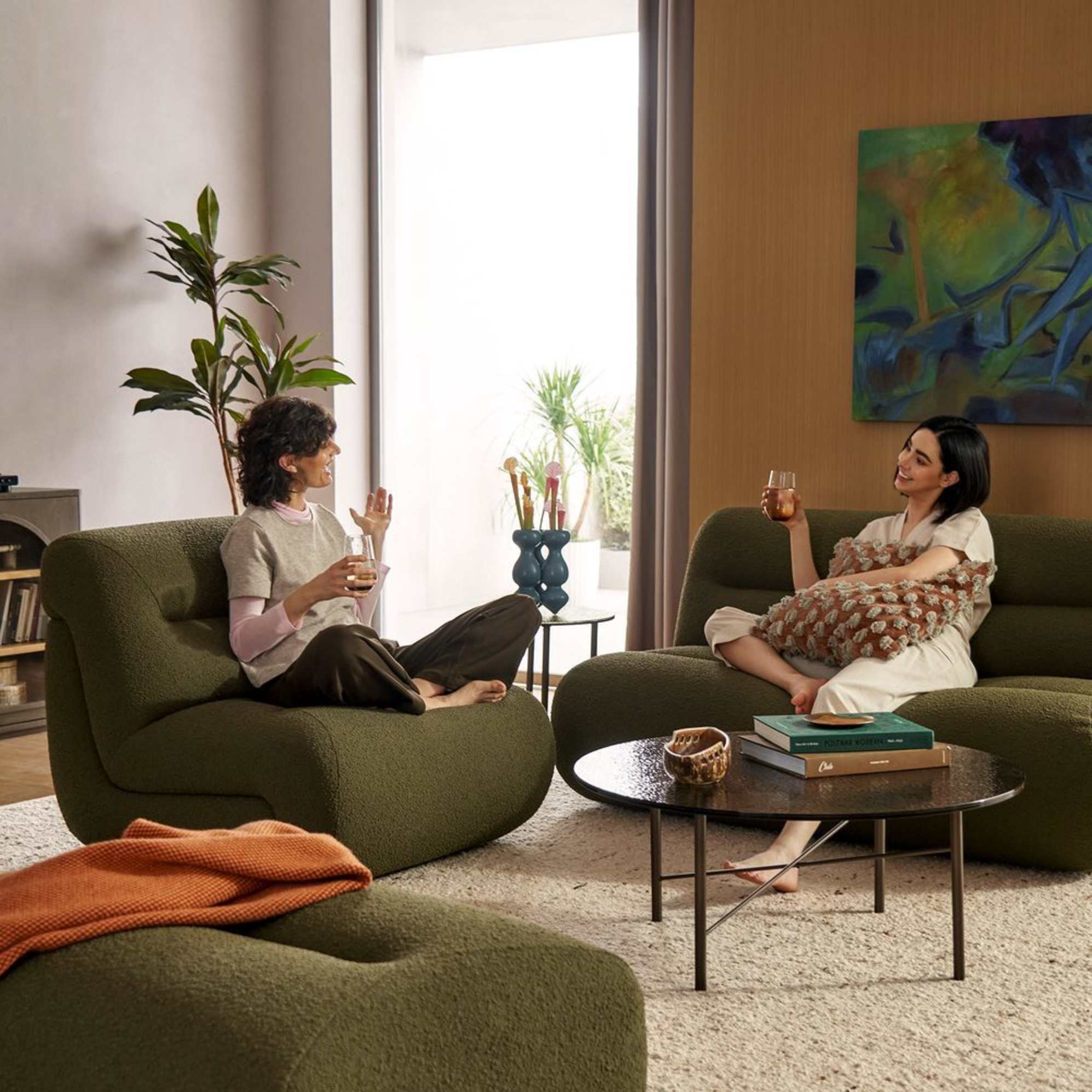 Two people sitting on a moss green modular armless sofa.