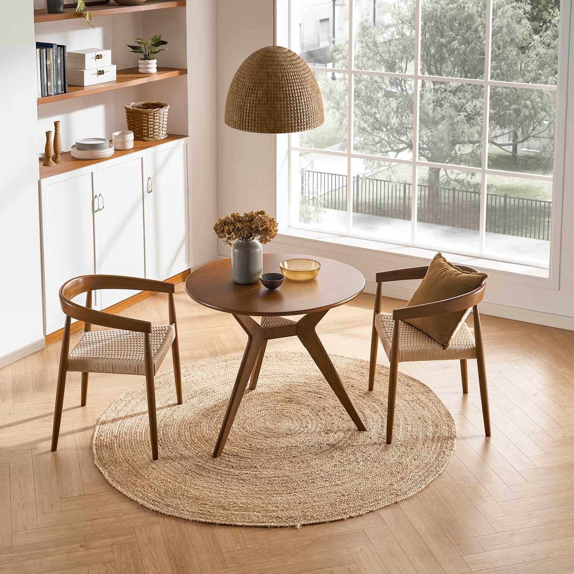 Two matching woven dining arm chairs with a round dining table placed between them. 