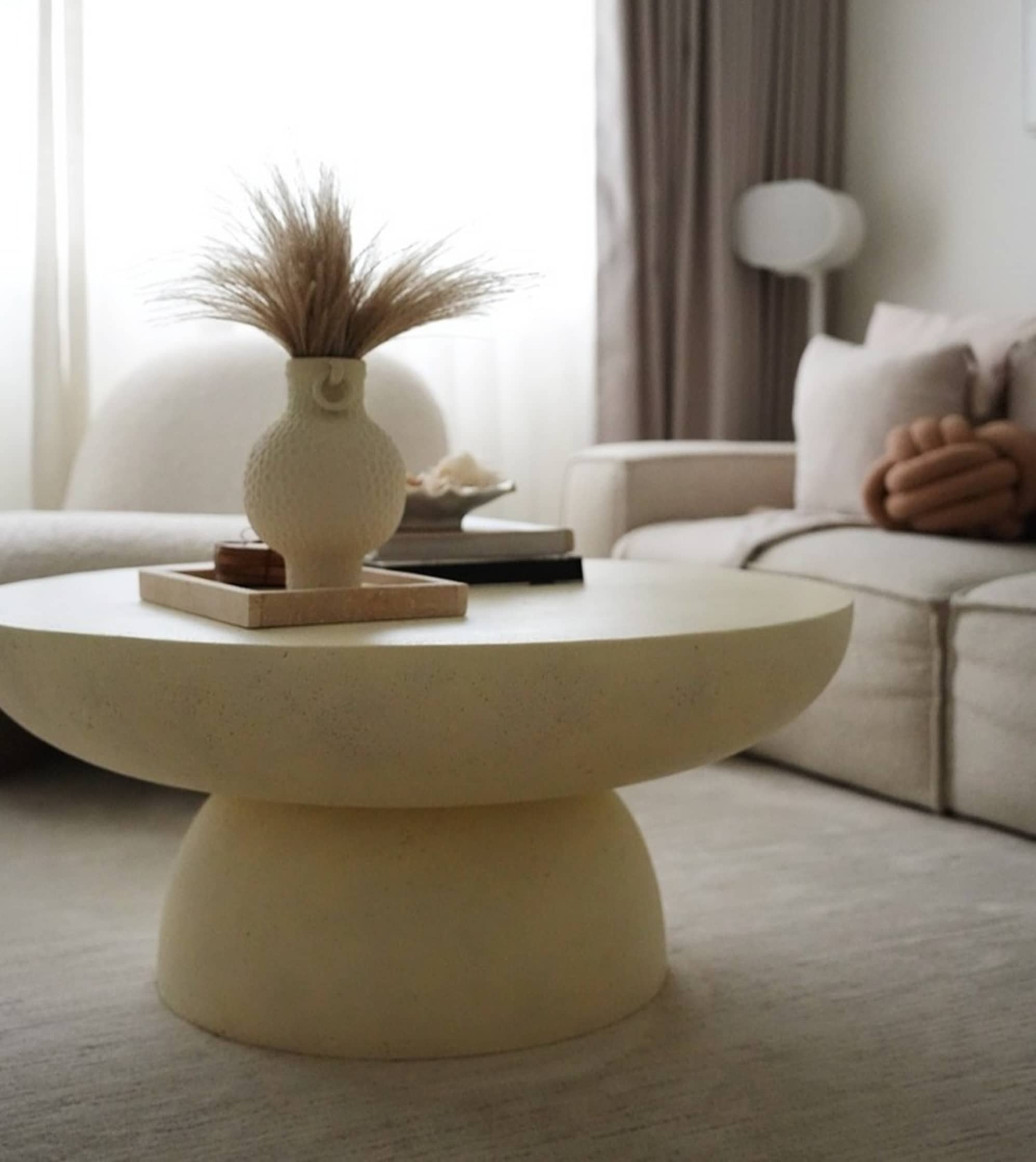 A round coffee table with a tray, vase, and books placed on its surface.