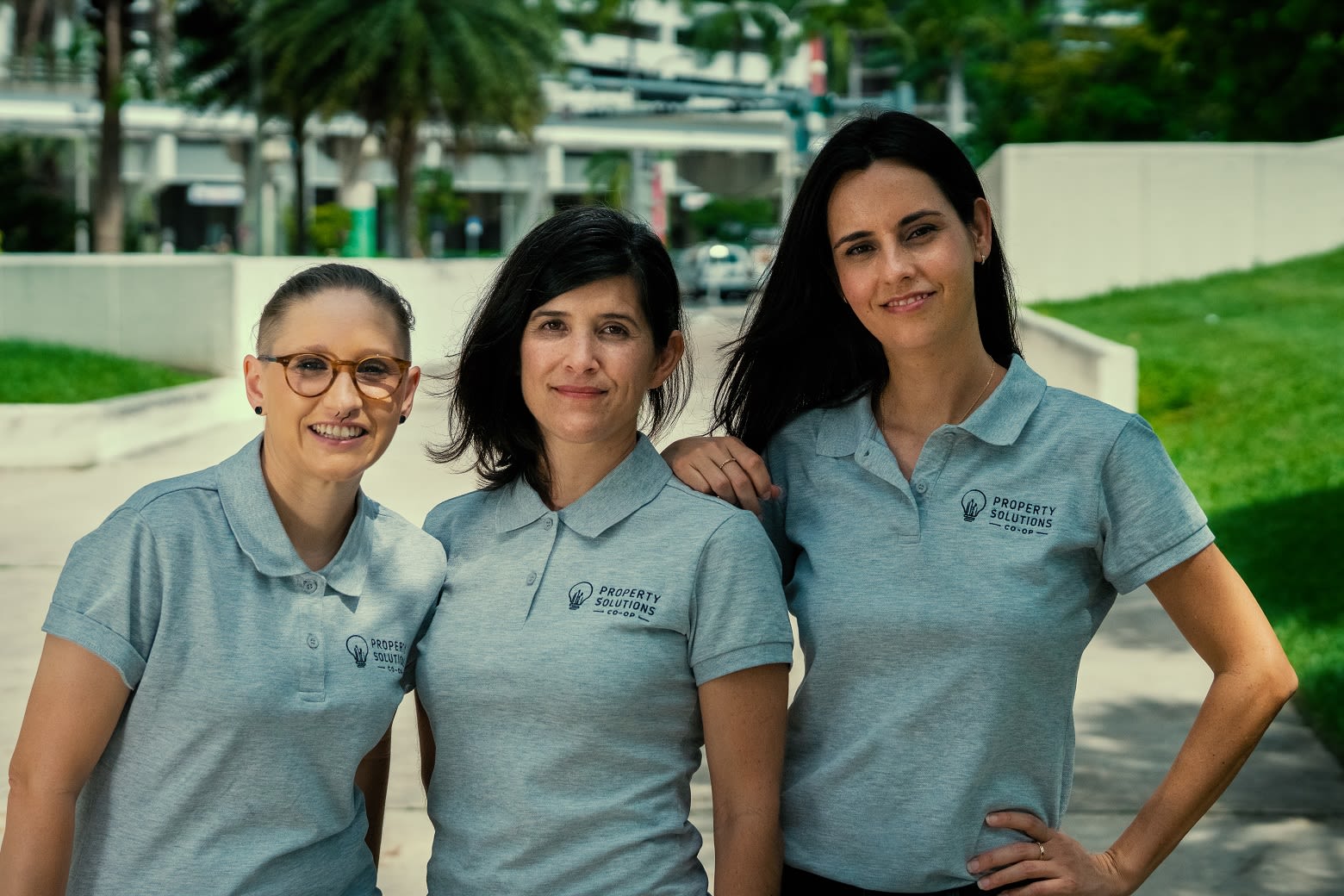 L to R: Jessica, Ilyana and Caara standing outside, posing and smiling, wearing their Property Solutions Co-op uniform