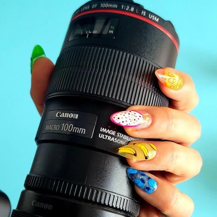 A client holds a camera and shows off her custom acrylics designed with different kinds of fruit.