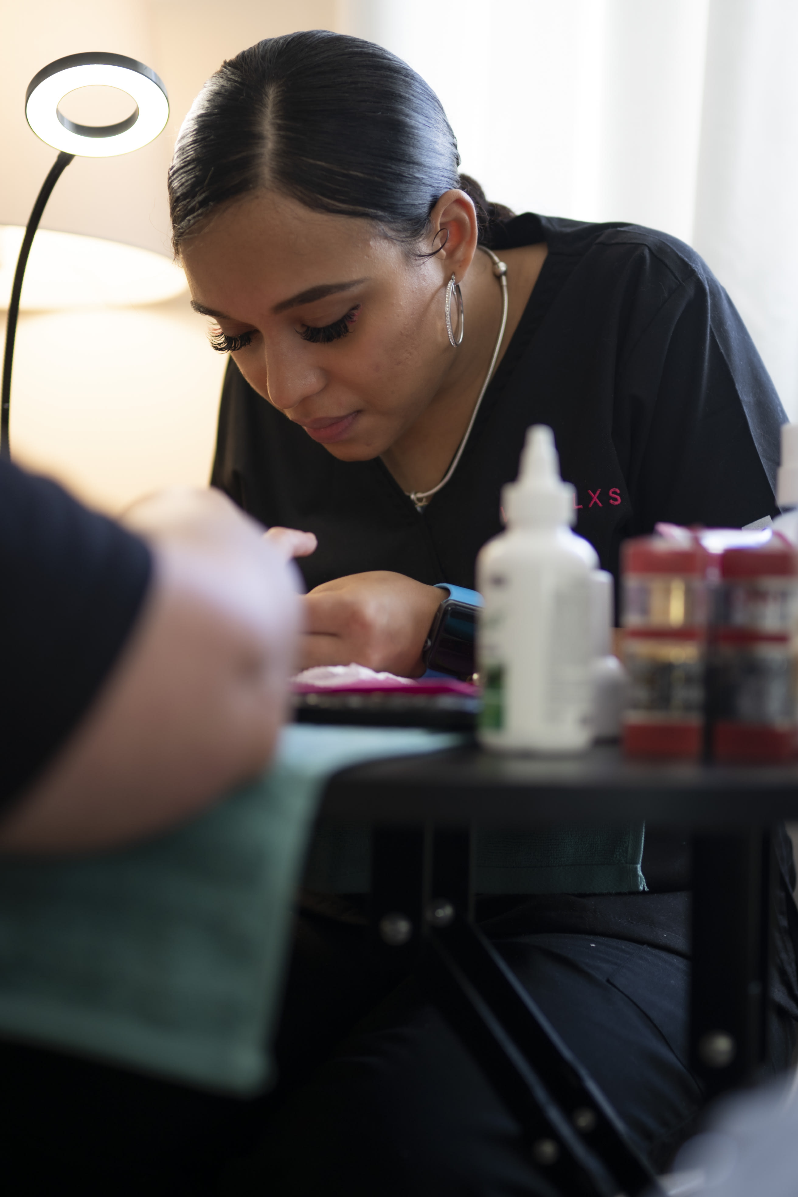 Vanessa Ramos, a brown-skinned Puerto Rican woman bens over a client's hands while she does their nails.