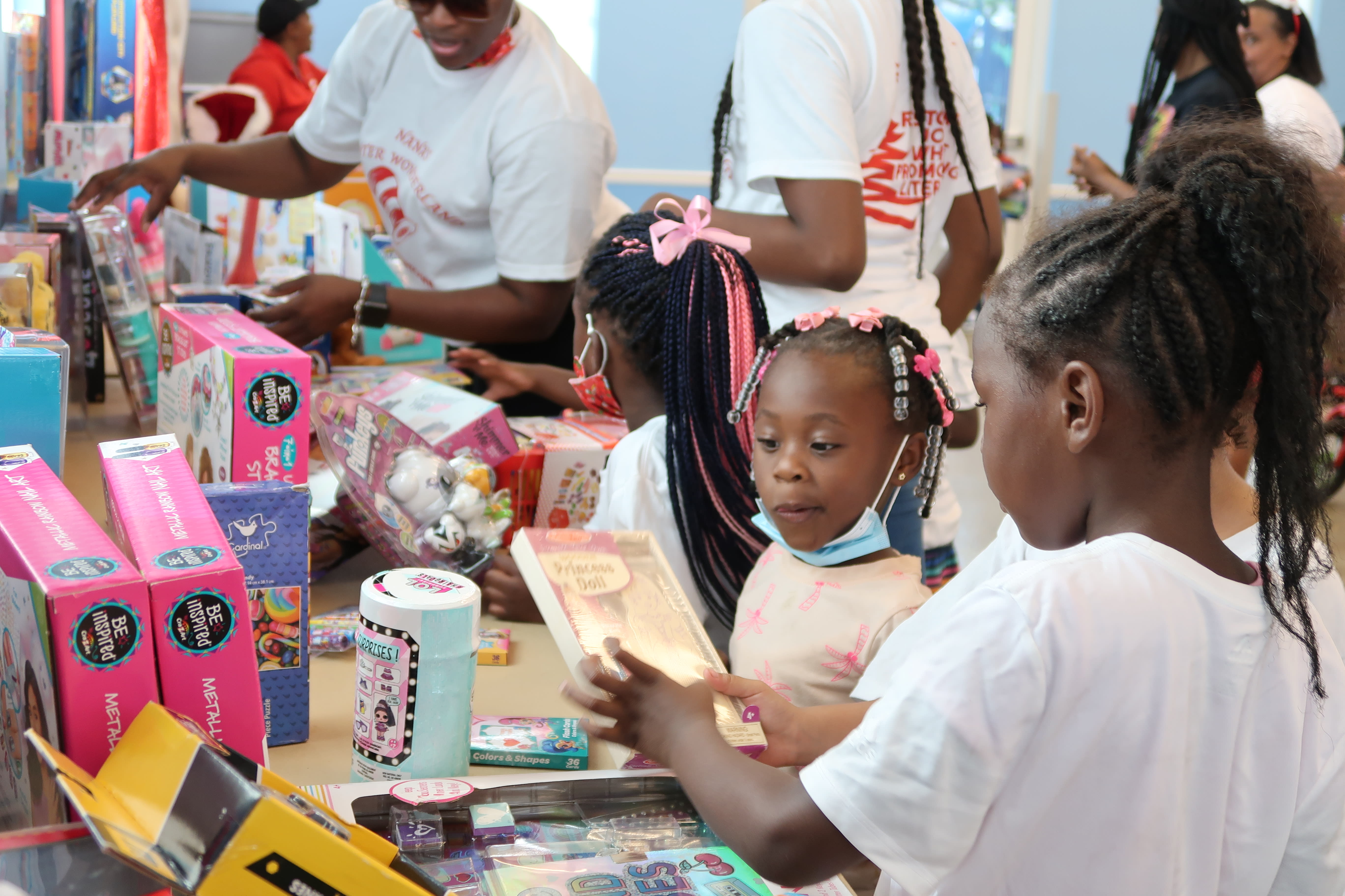 Three young black girls with bows in their hair look at the free gifts they can choose from.