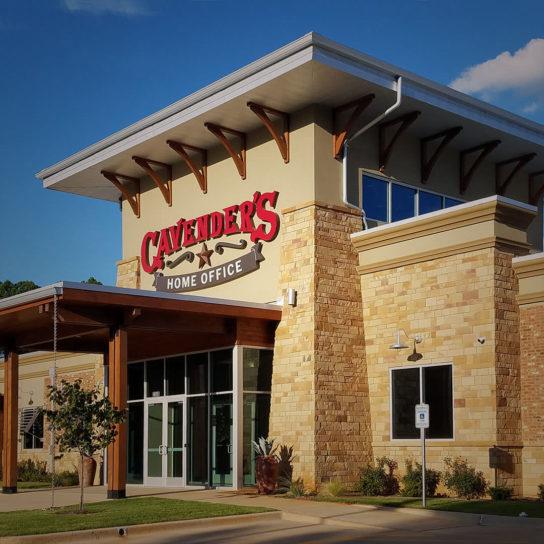 The image depicts Cavender’s new office in Tyler, TX, showcasing a modern design that blends stone and wood elements. The prominent Cavender’s sign indicates its role as the company’s new hub. This opening, during the challenging times of the COVID-19 pandemic, highlights Cavender’s commitment to serving the community by providing essential work wear through its stores.