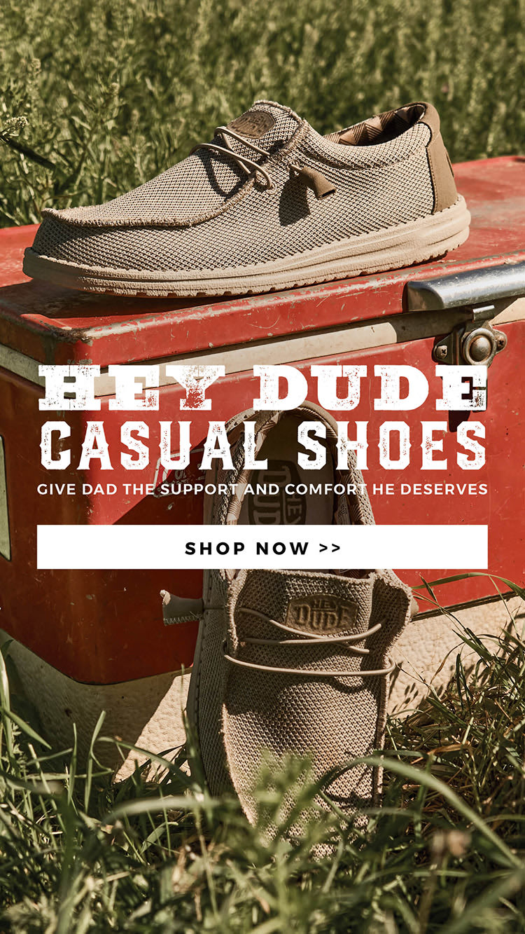 Banner showing a pair of Hey Dude casual shoes with an old ice chest in tall grass. Textured white text reads "HEY DUDE CASUAL SHOES GIVE DAD THE SUPPORT AND COMFORT HE DESERVES". Click to shop