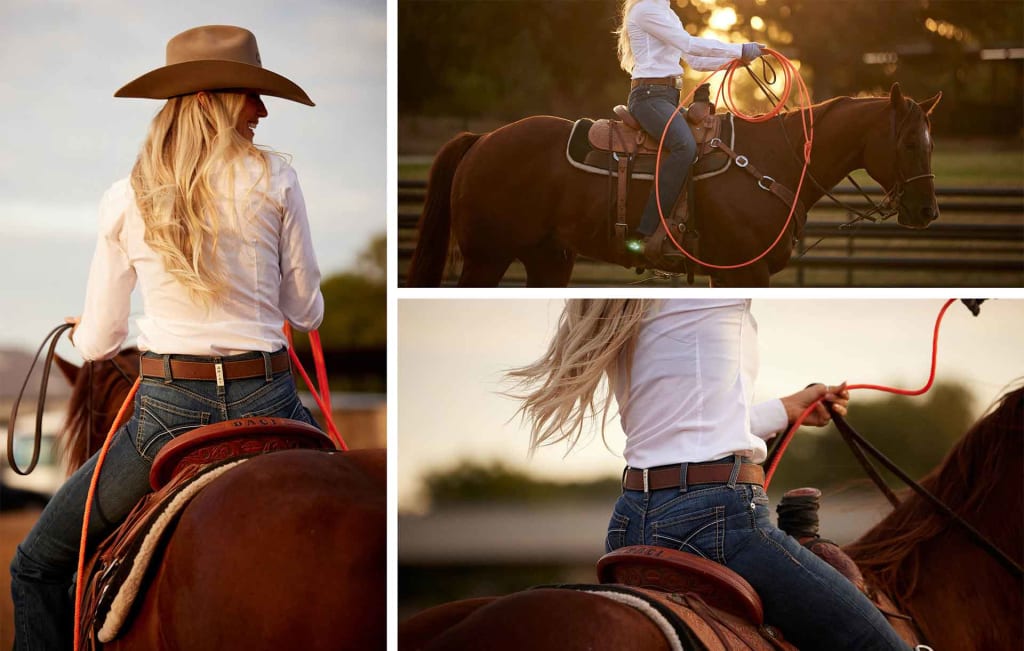 Ariat Women's Denim Belt Loop Detail: showing a cowgirl riding her horse, smiling with her felt cowboy hat on as she starts to to rope.