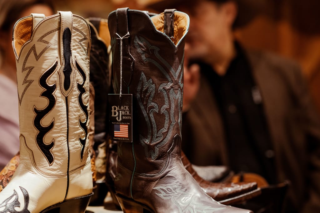 Black Jack Boots elegantly displayed on a carousel table, showcasing a striking contrast between sleek white and rich brown leather, highlighting their refined shine.