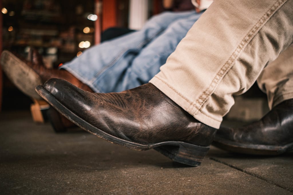 Image of a man in light khaki jeans showing off a pair of brown leather dress boots.