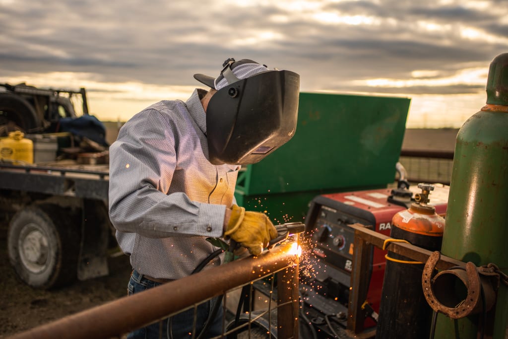 Skilled farmer welding on the farm under a partly cloudy sky.