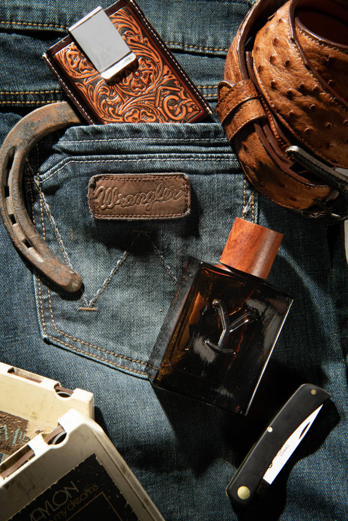 Collage of Western Accessories: Folded Western Jeans with Horseshoe, Exotic Belt, Leather Money Clip Wallet, Cologne, and Pocket Knife.